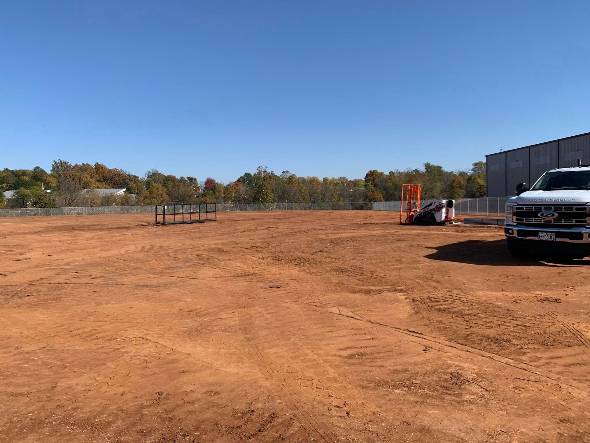 Empty dirt lot beside a building, with a pickup truck parked on the right under a clear blue sky.