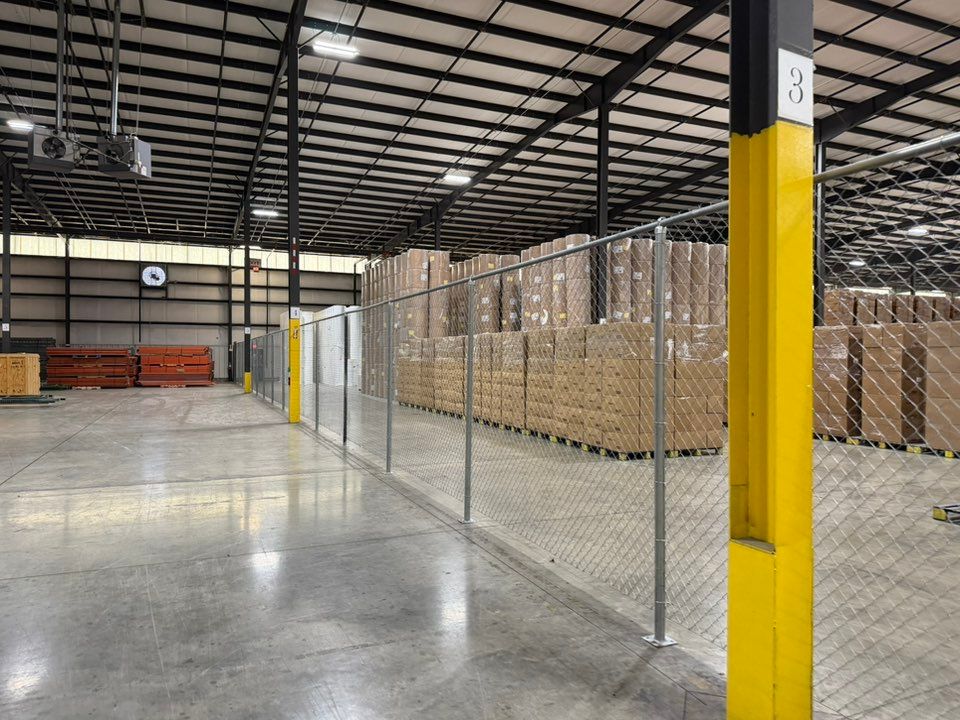 Warehouse aisle with chain-link fencing, stacked boxes, and yellow support columns on a polished concrete floor