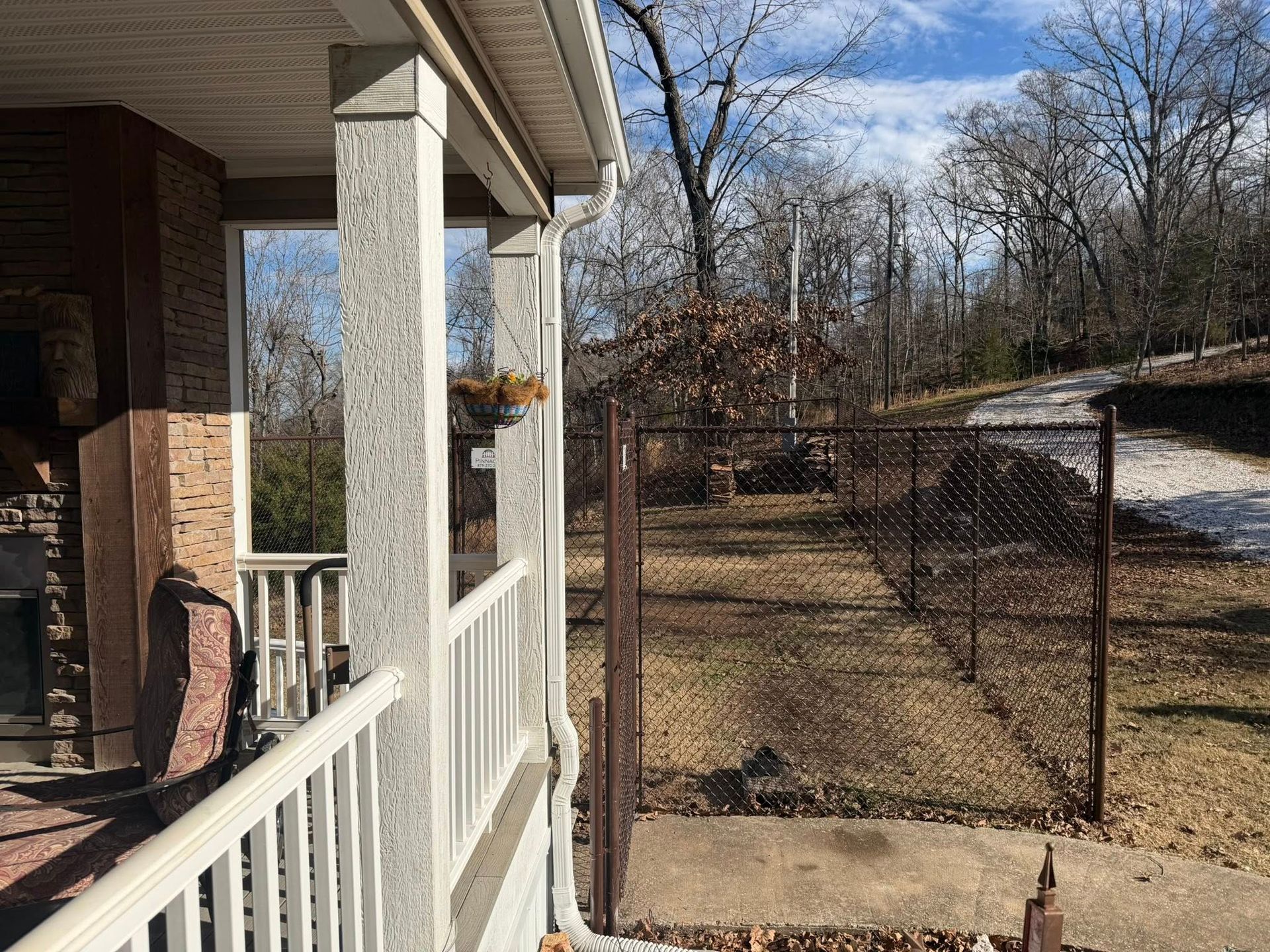 Front porch with white railing overlooking a fenced yard and leafless trees on a clear day