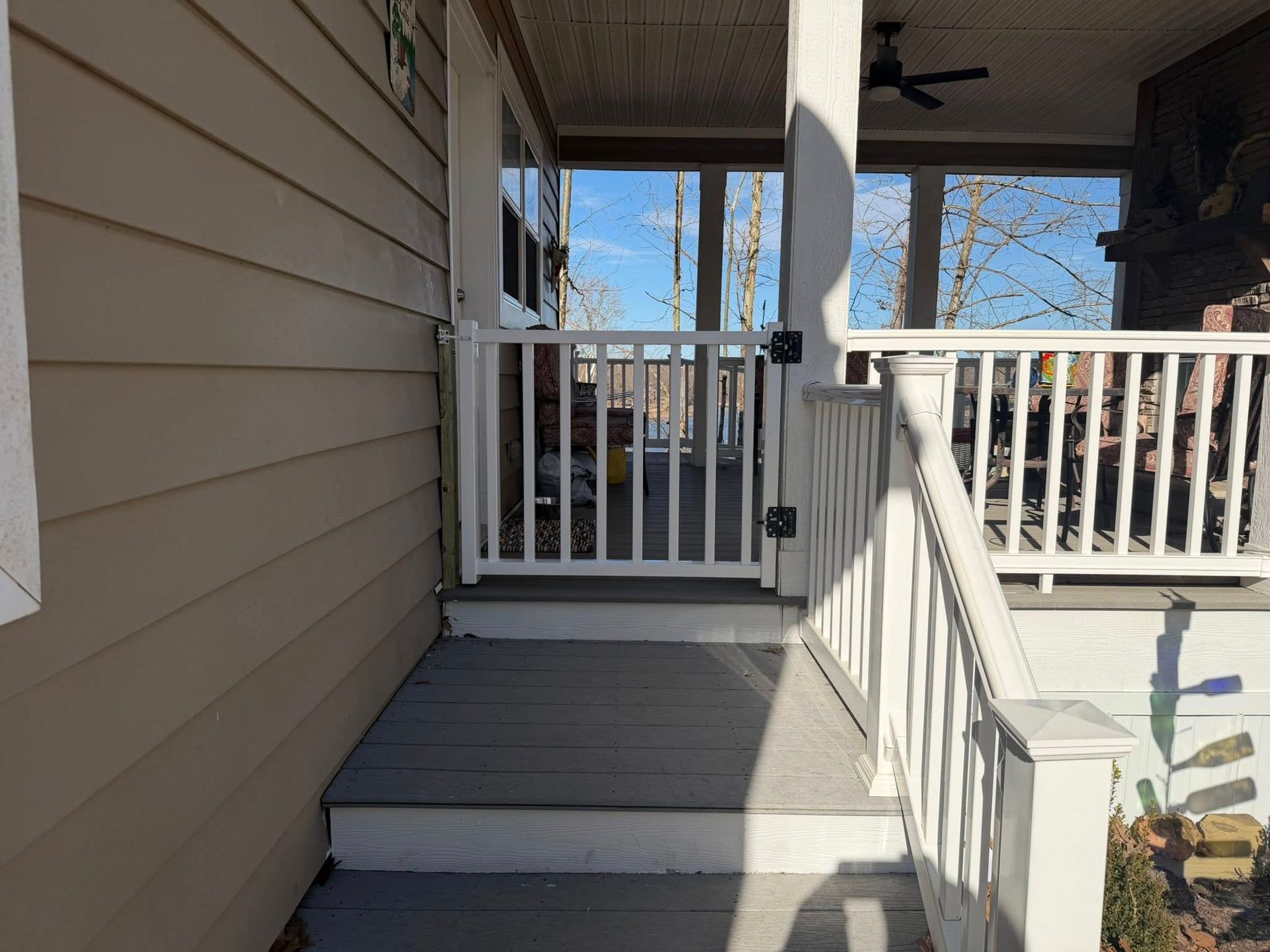 Covered front porch with gray steps, white railing, and tan siding in daylight.