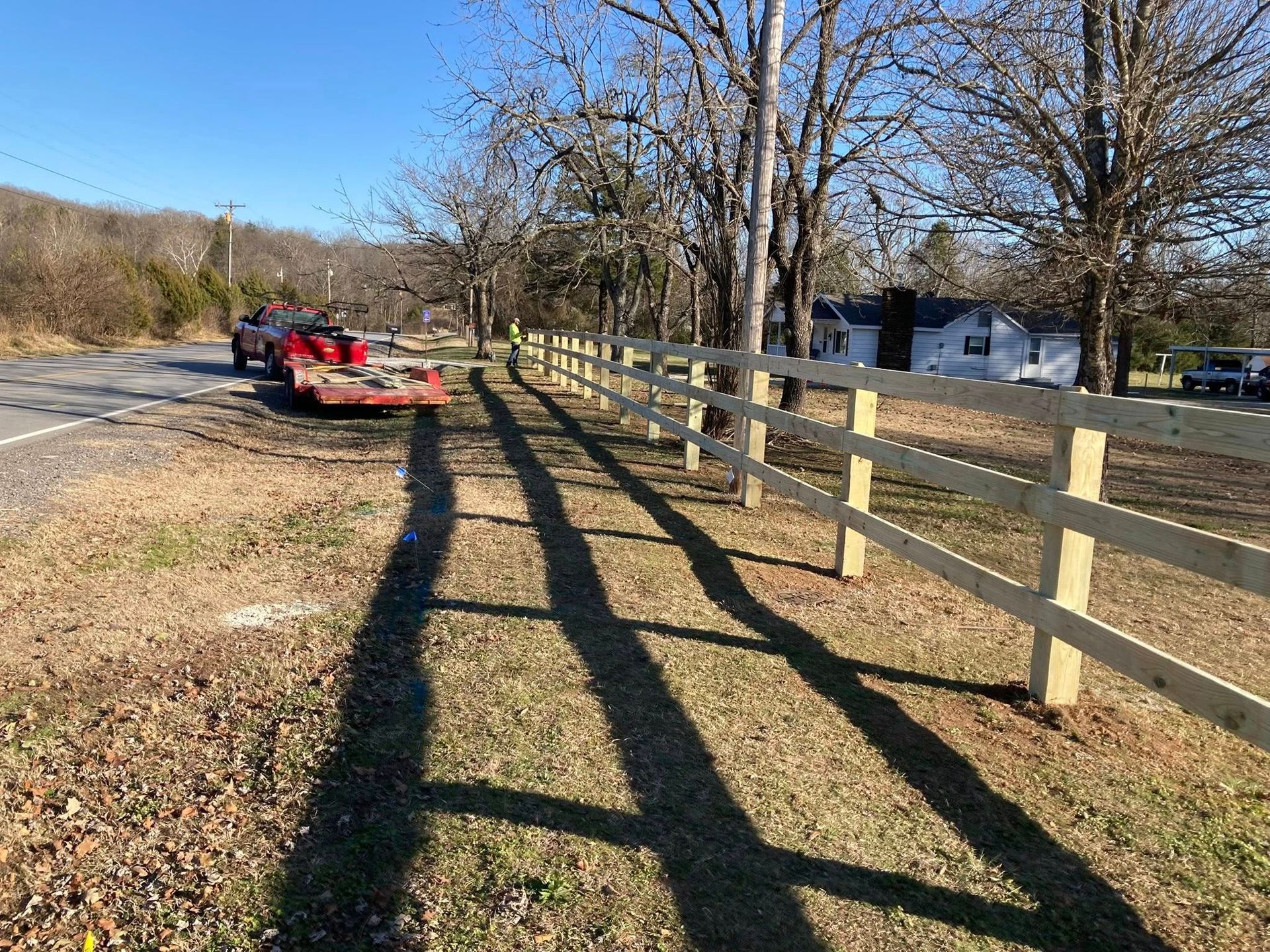 Red mower parked by a roadside with long fence shadows across a grassy path on a sunny day