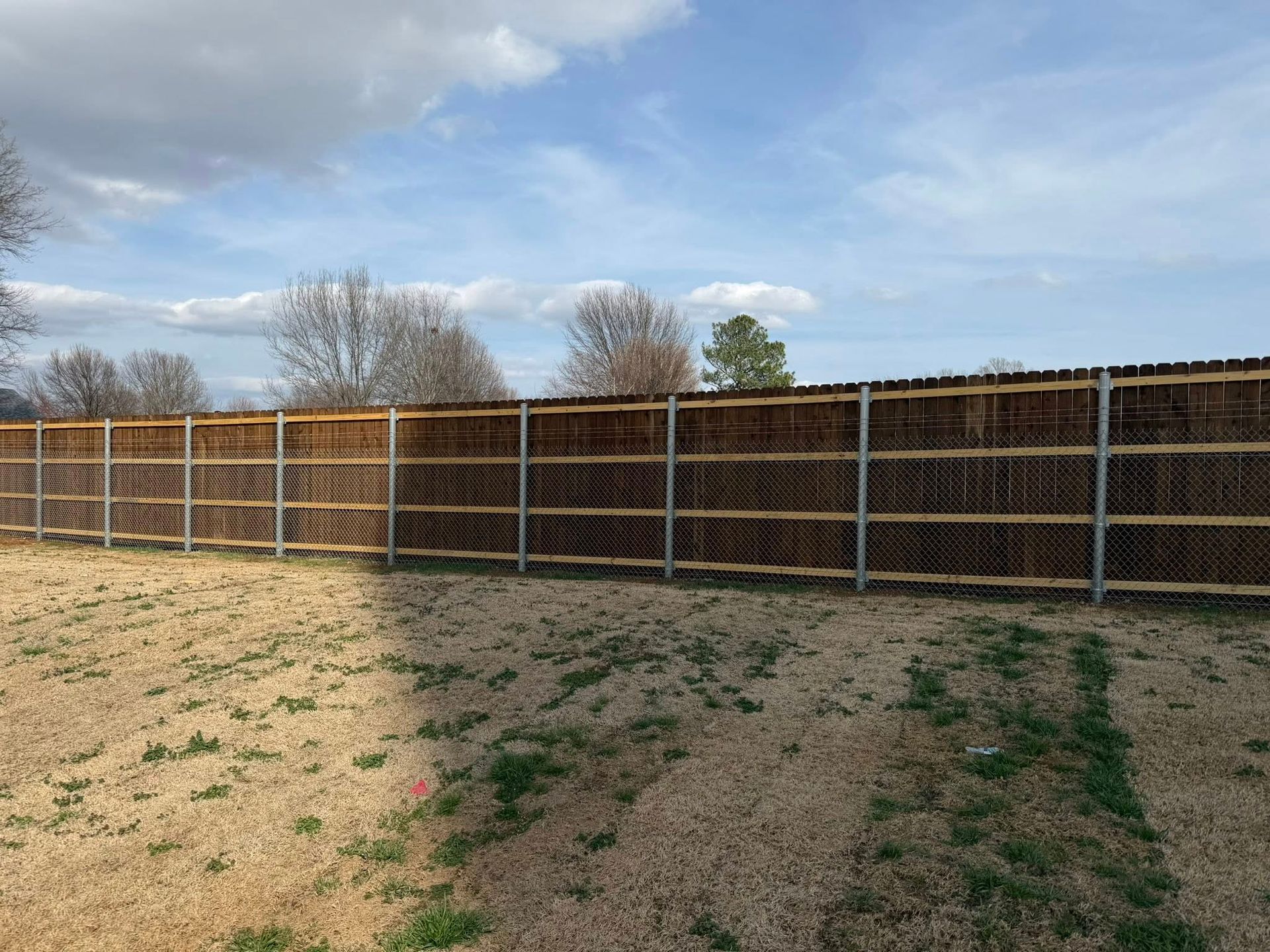 Long wooden fence beside a sandy field under a cloudy sky