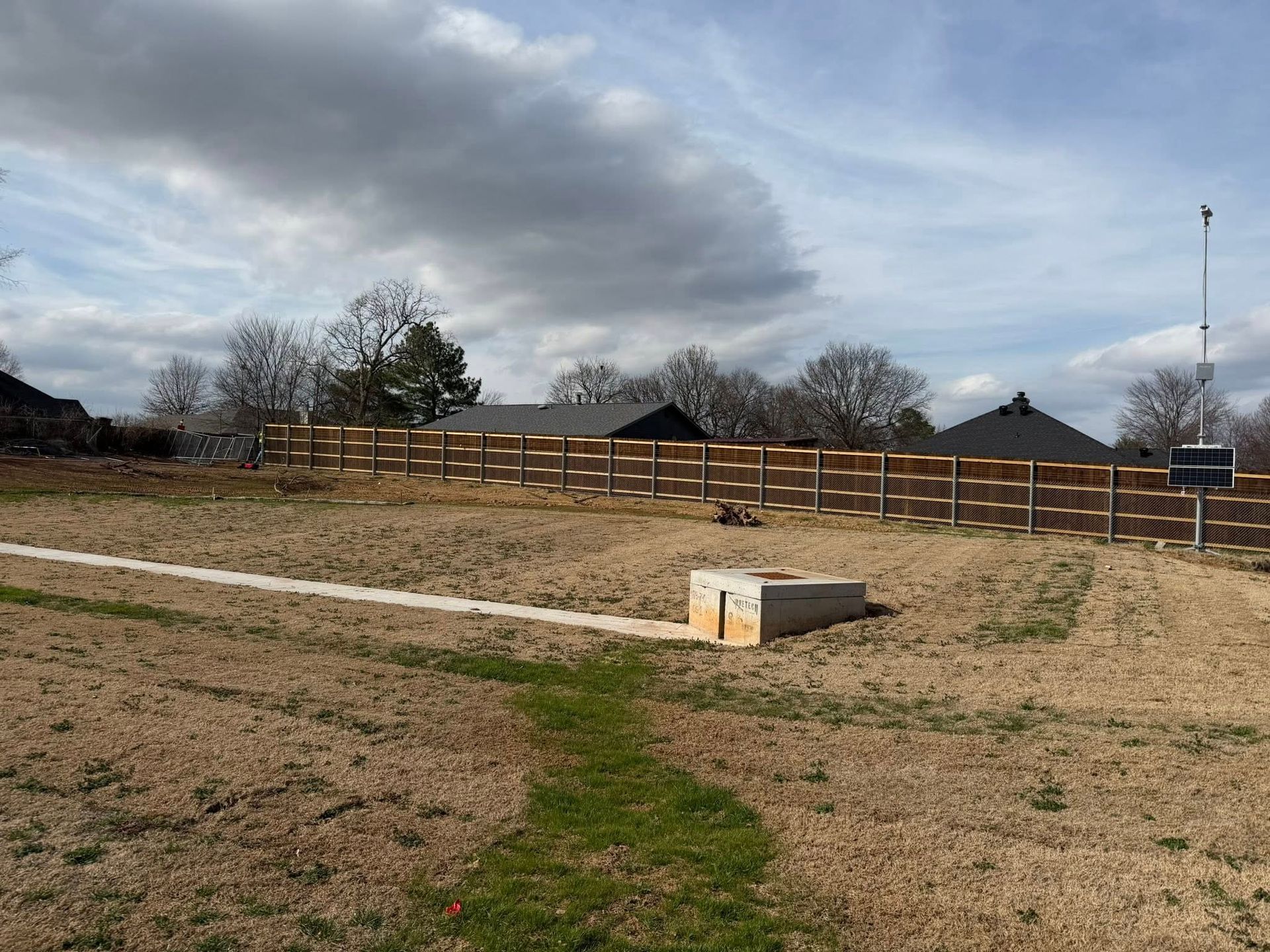 Open field with a wooden fence under a cloudy sky, with a small concrete bench in the foreground