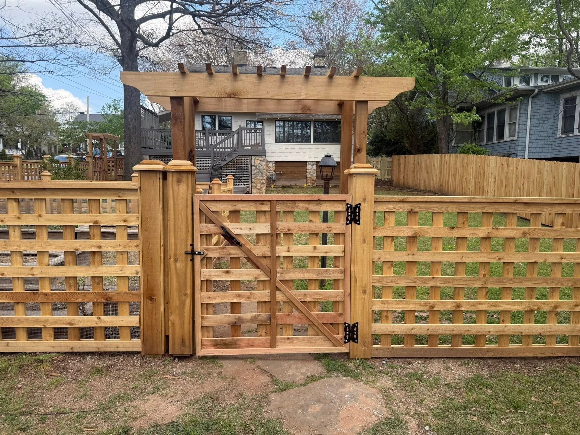 Wooden backyard fence with a center gate and pergola-style top, set between neighboring houses.
