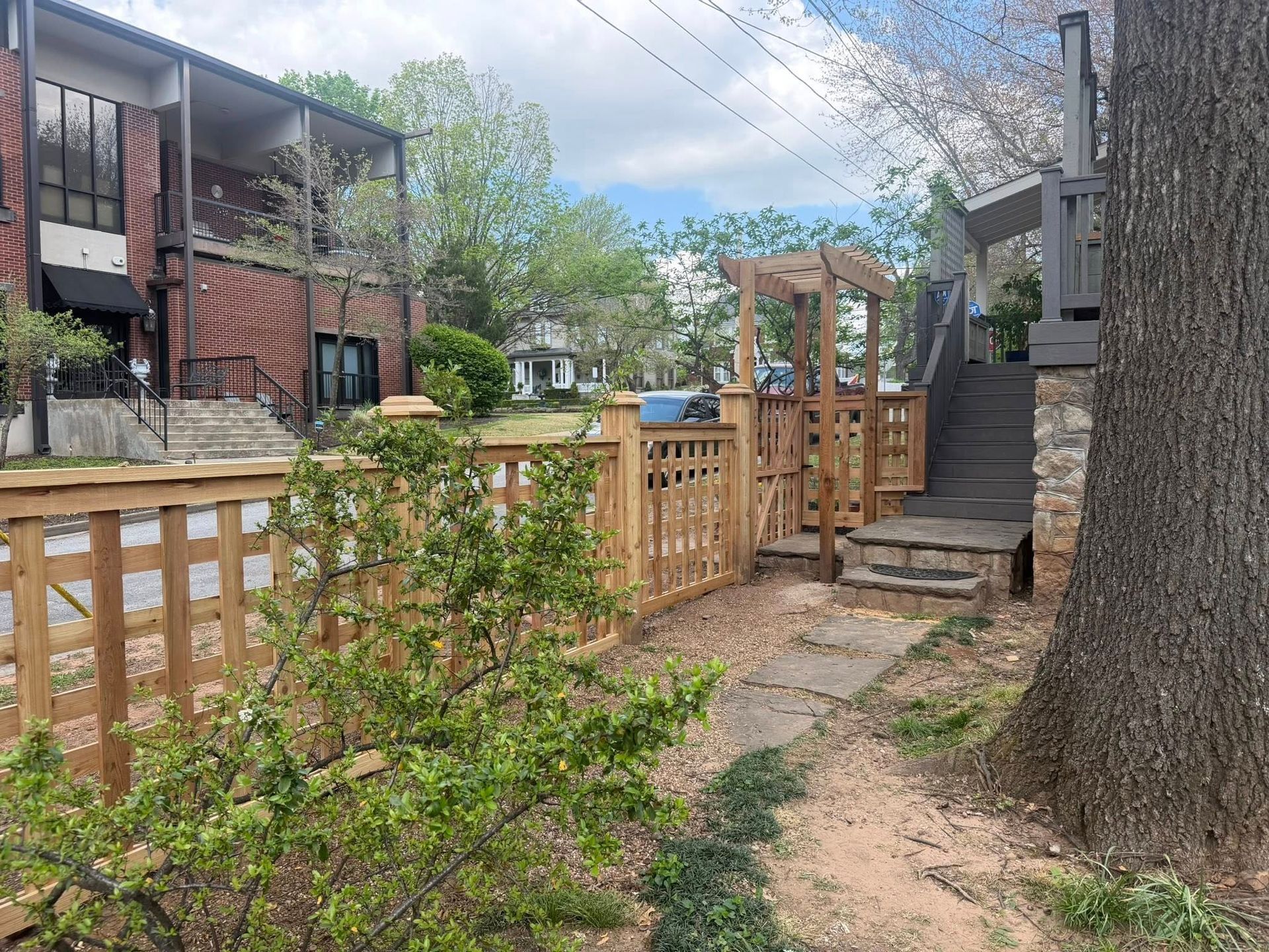 Backyard wooden fence and gate beside apartment buildings, with steps and a dirt path under trees.