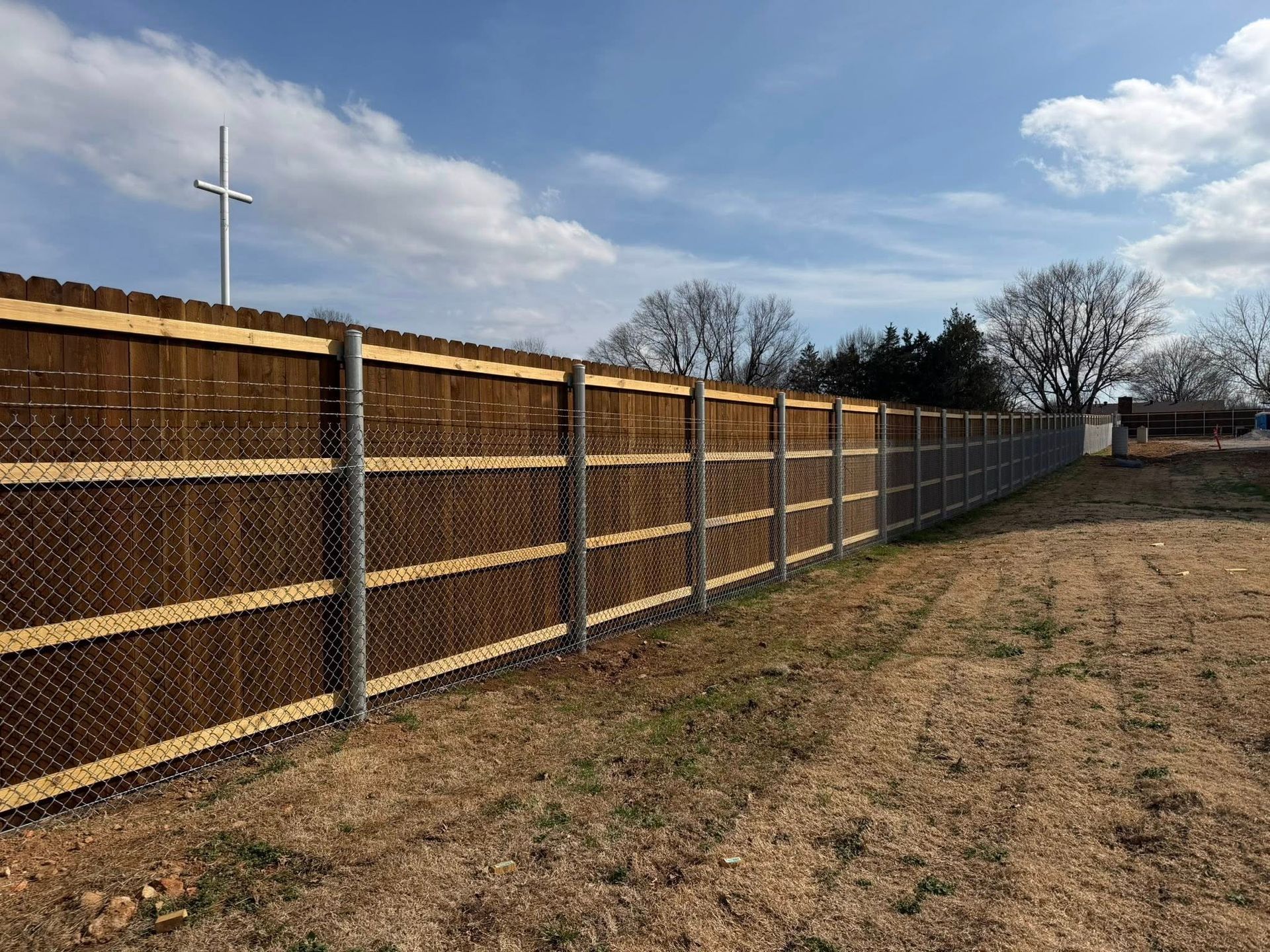Long wooden privacy fence along a grassy field under a partly cloudy sky