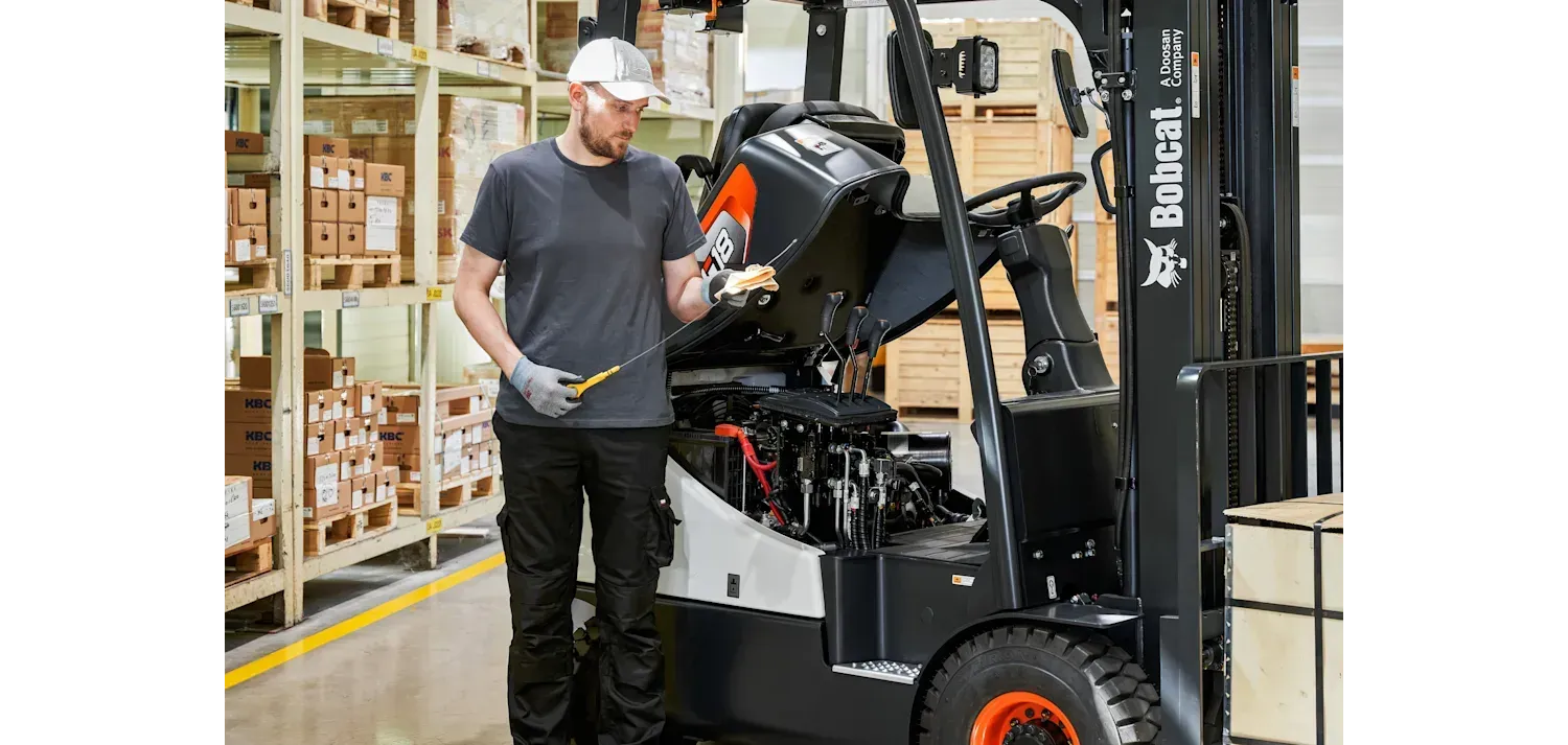 A man is working on a forklift in a warehouse.