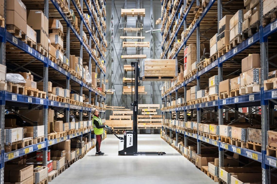 A man is standing in a warehouse loading boxes on a forklift.