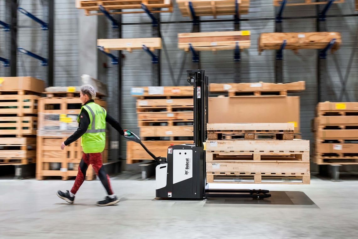 A man is pushing a forklift in a warehouse.
