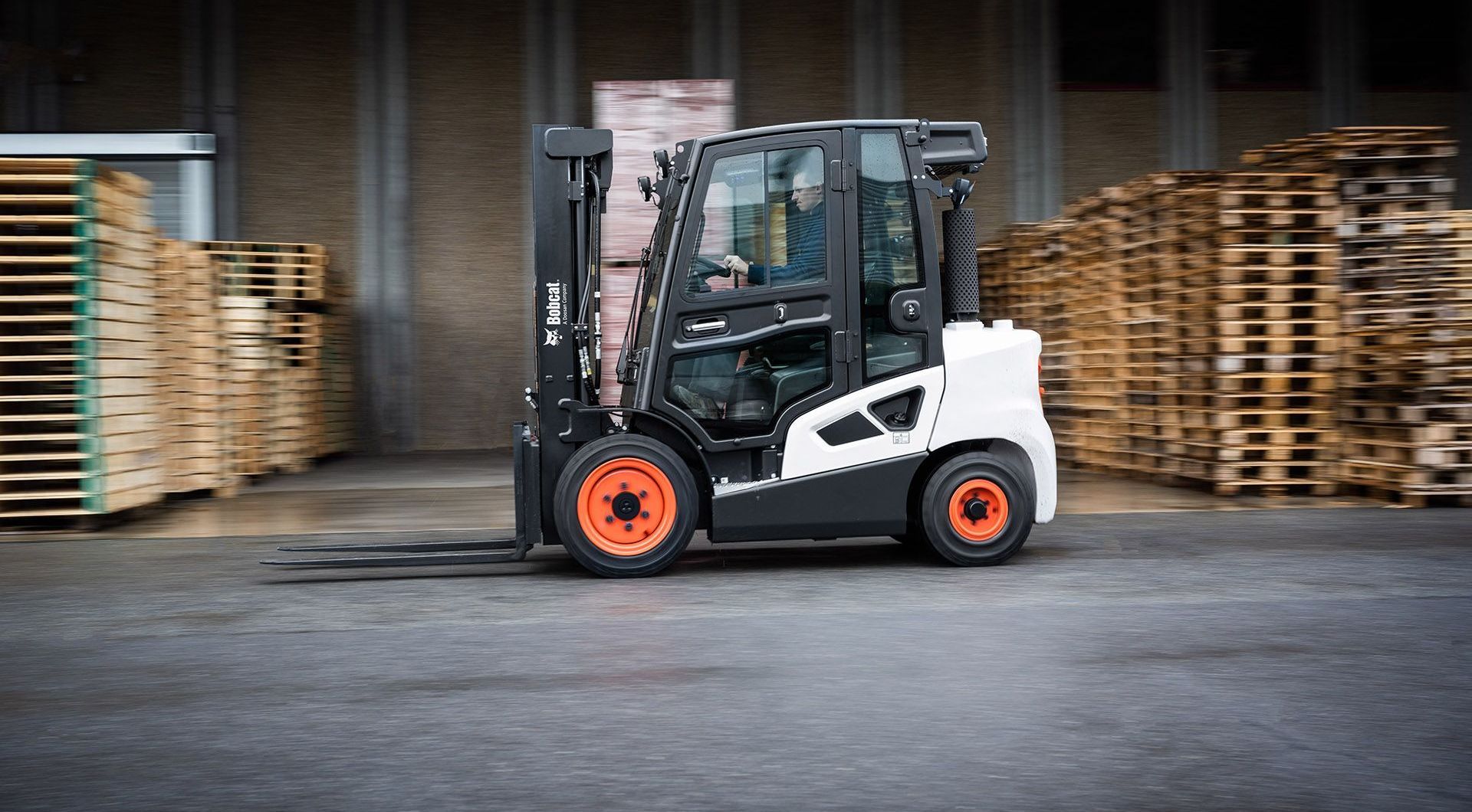 A forklift is driving through a warehouse filled with wooden pallets.