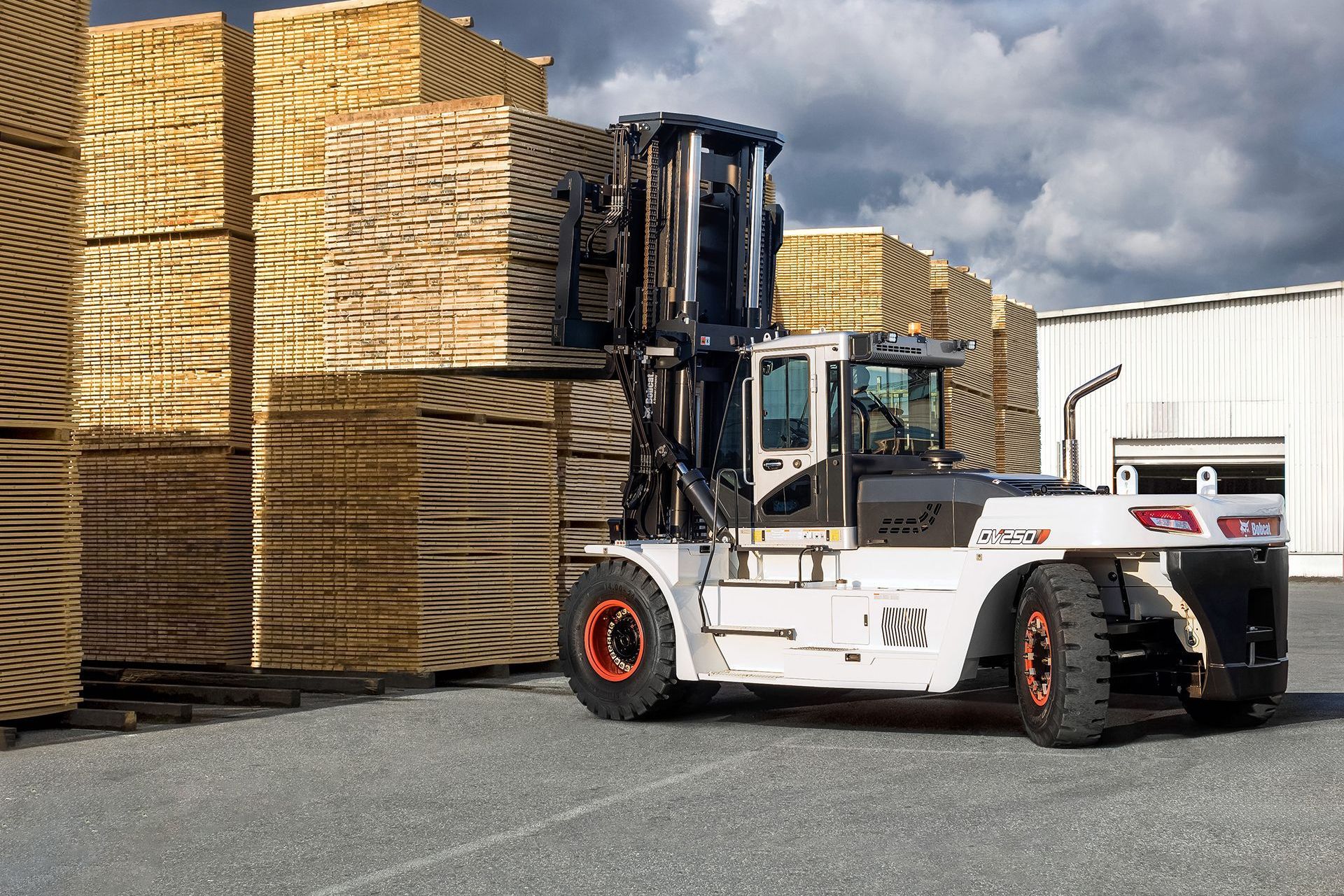 A forklift is carrying a stack of wood in a parking lot.