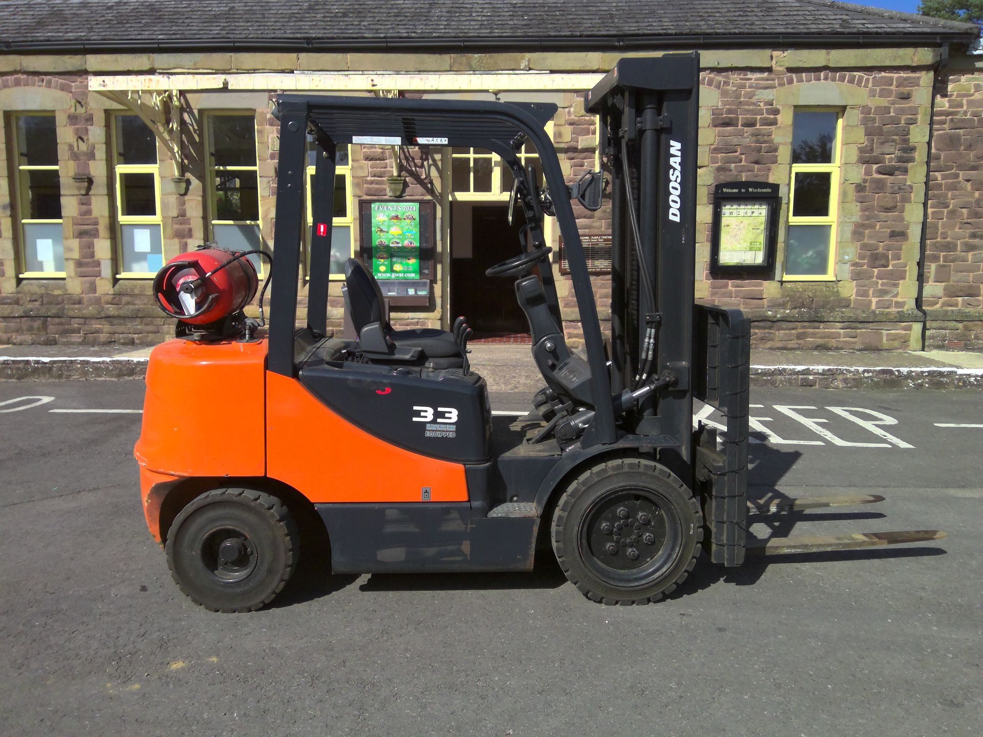 A doosan forklift is parked in front of a brick building