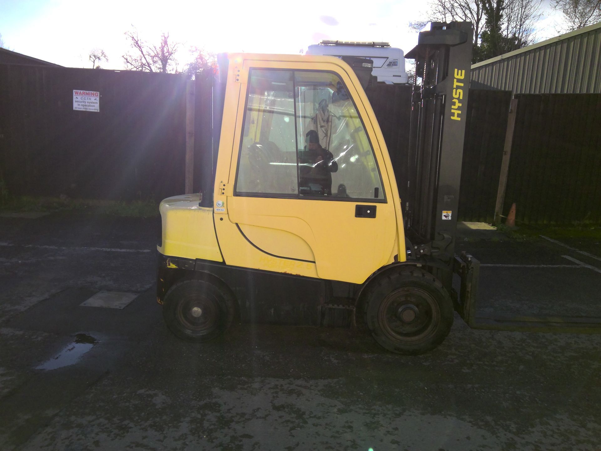 A yellow forklift is parked in front of a fence.