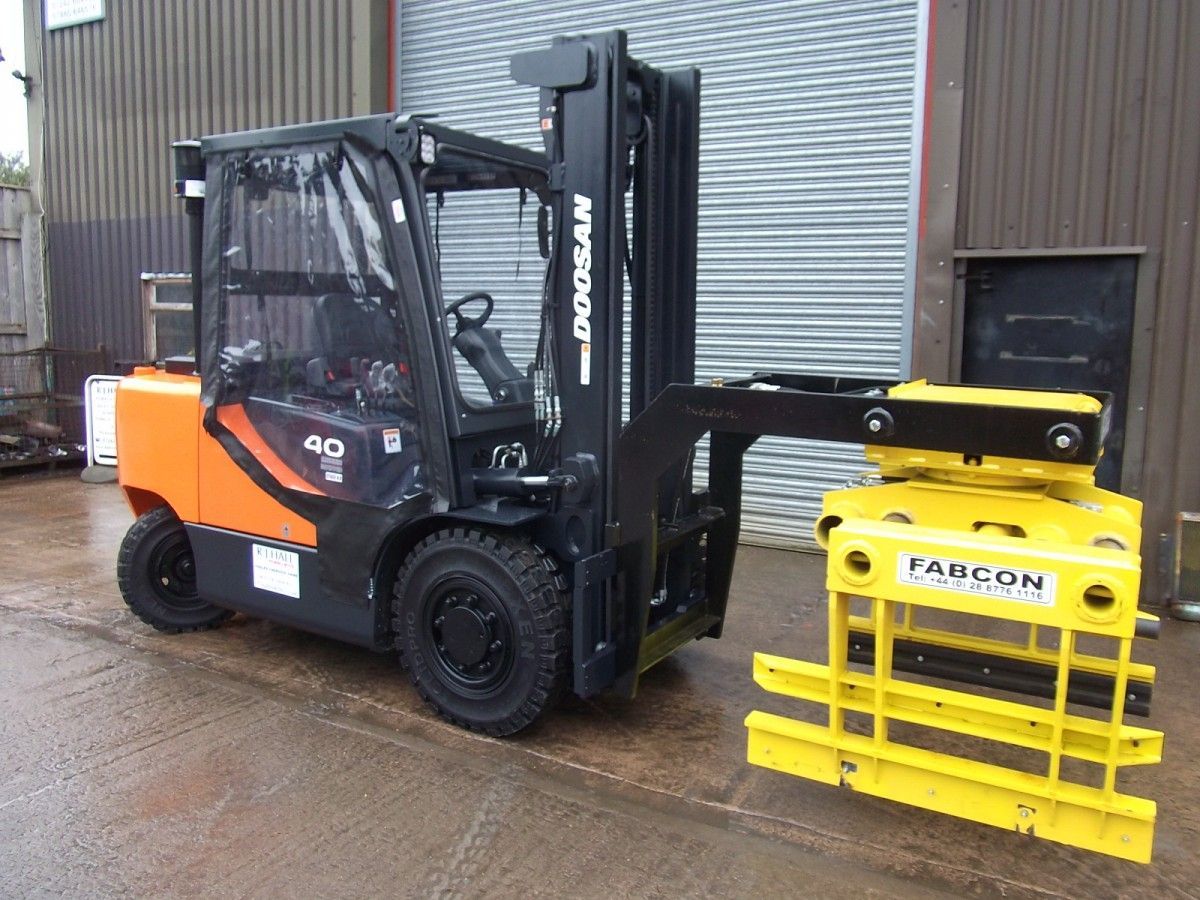 A forklift with a yellow clamp attached to it is parked in front of a building.