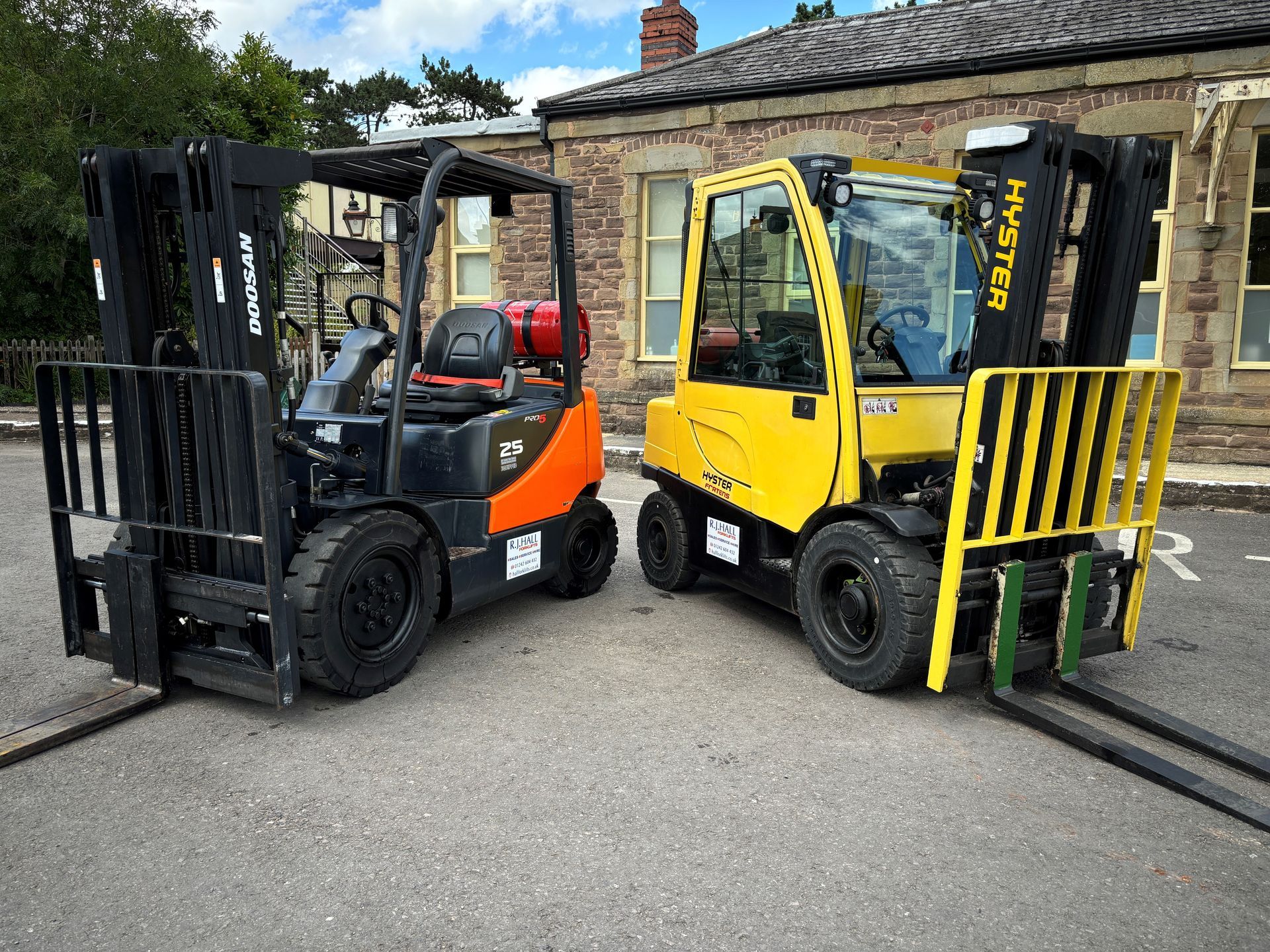 Two forklifts are parked next to each other in front of a building.