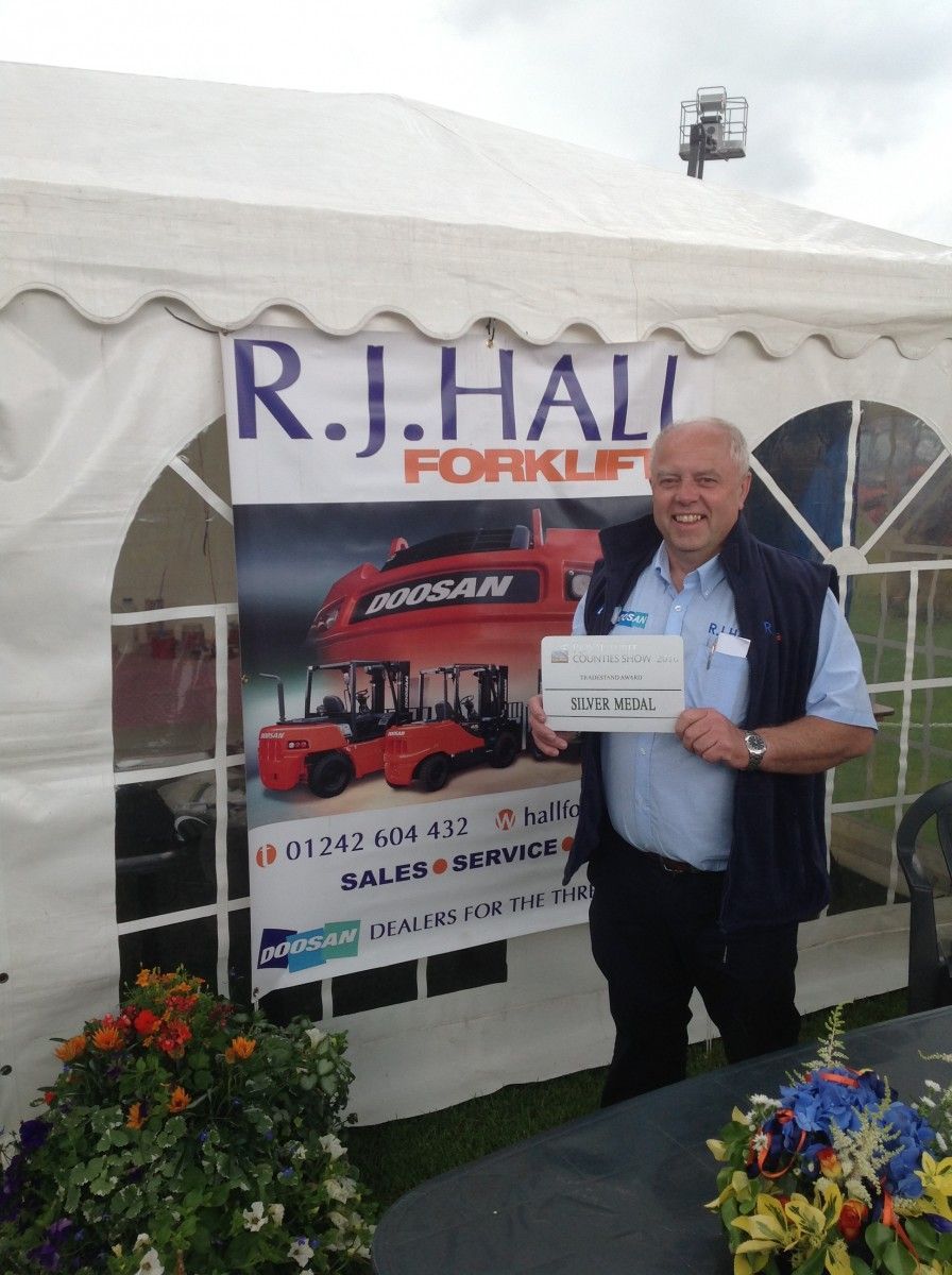 A man is standing in front of a tent that says r.j. hall forklift
