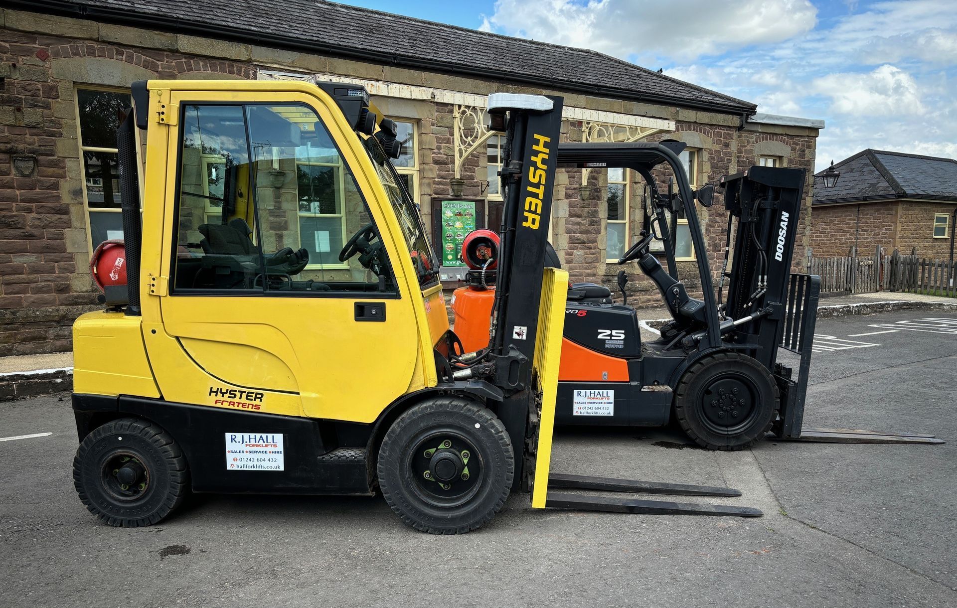 Two forklifts are parked in front of a brick building awaiting inspection