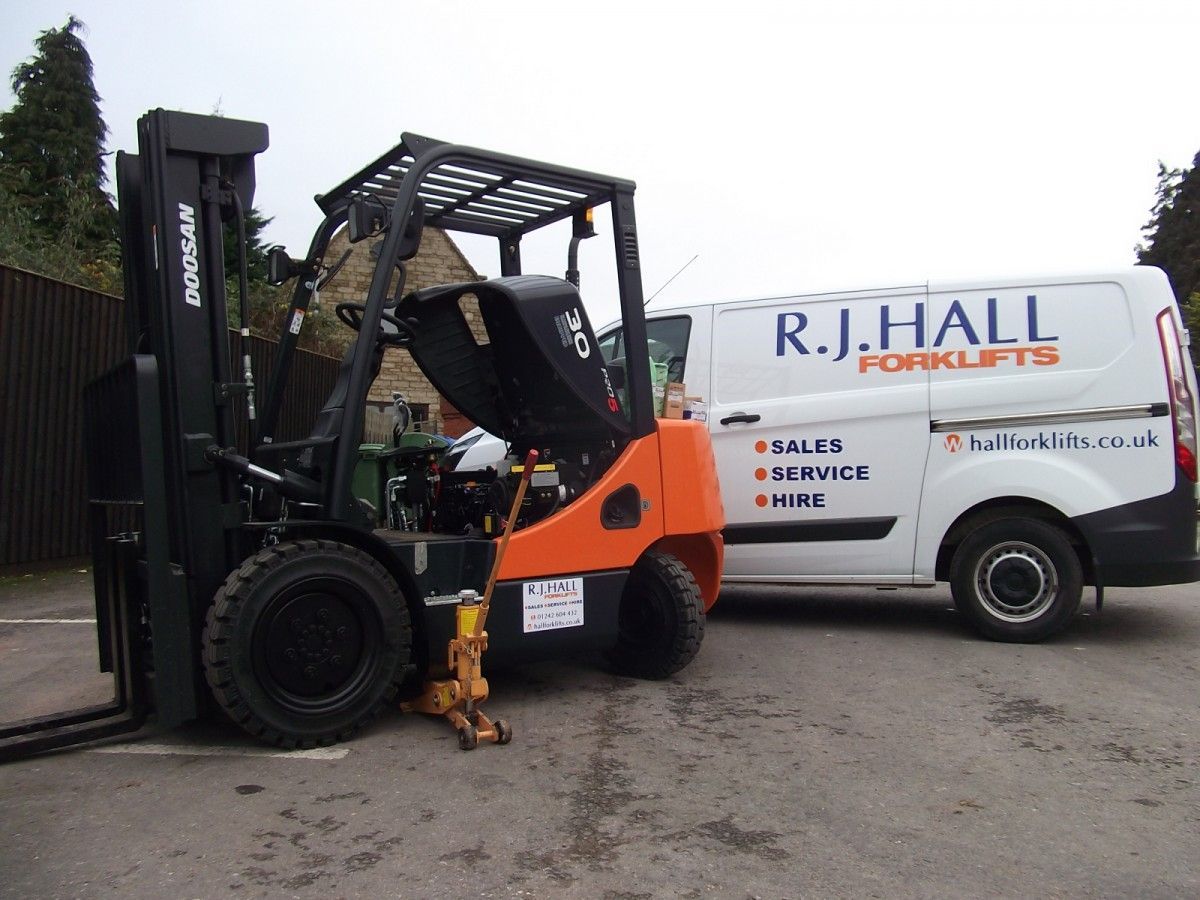 A forklift is parked next to a r.j. hall van