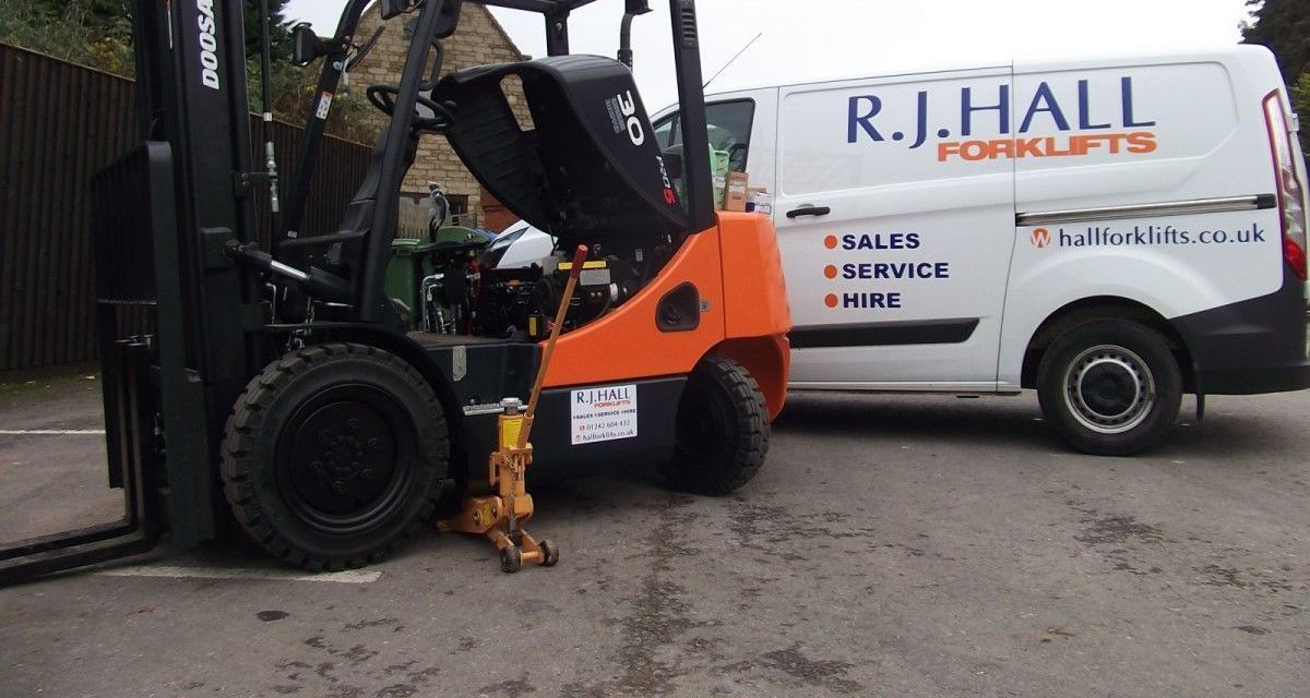 A forklift is parked next to a white van that says r.j. hall forklifts