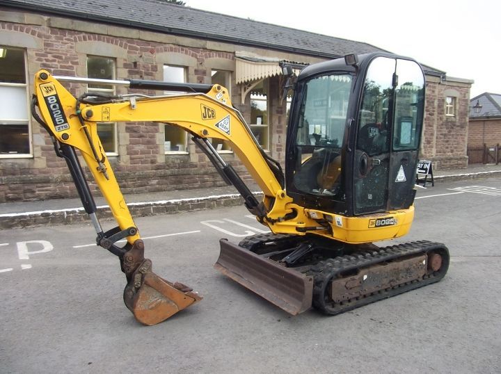 A small yellow excavator is parked in front of a building