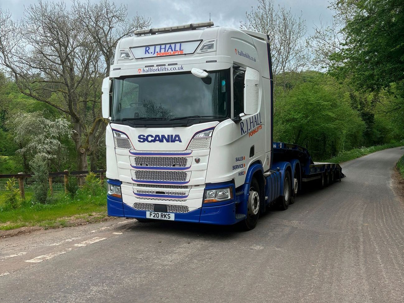 A blue and white scania semi truck is parked on the side of a road.