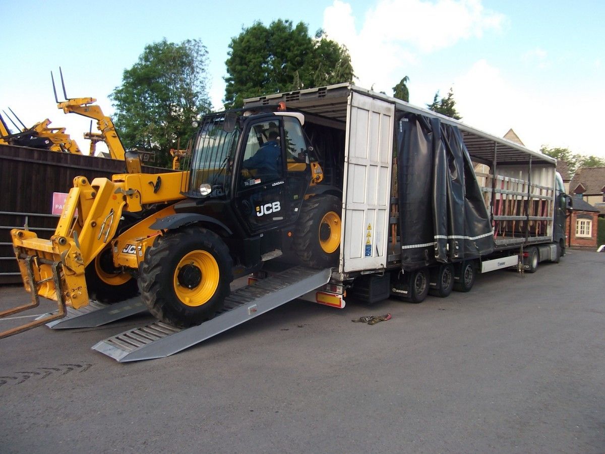 A yellow and black jcb tractor is being loaded into a trailer