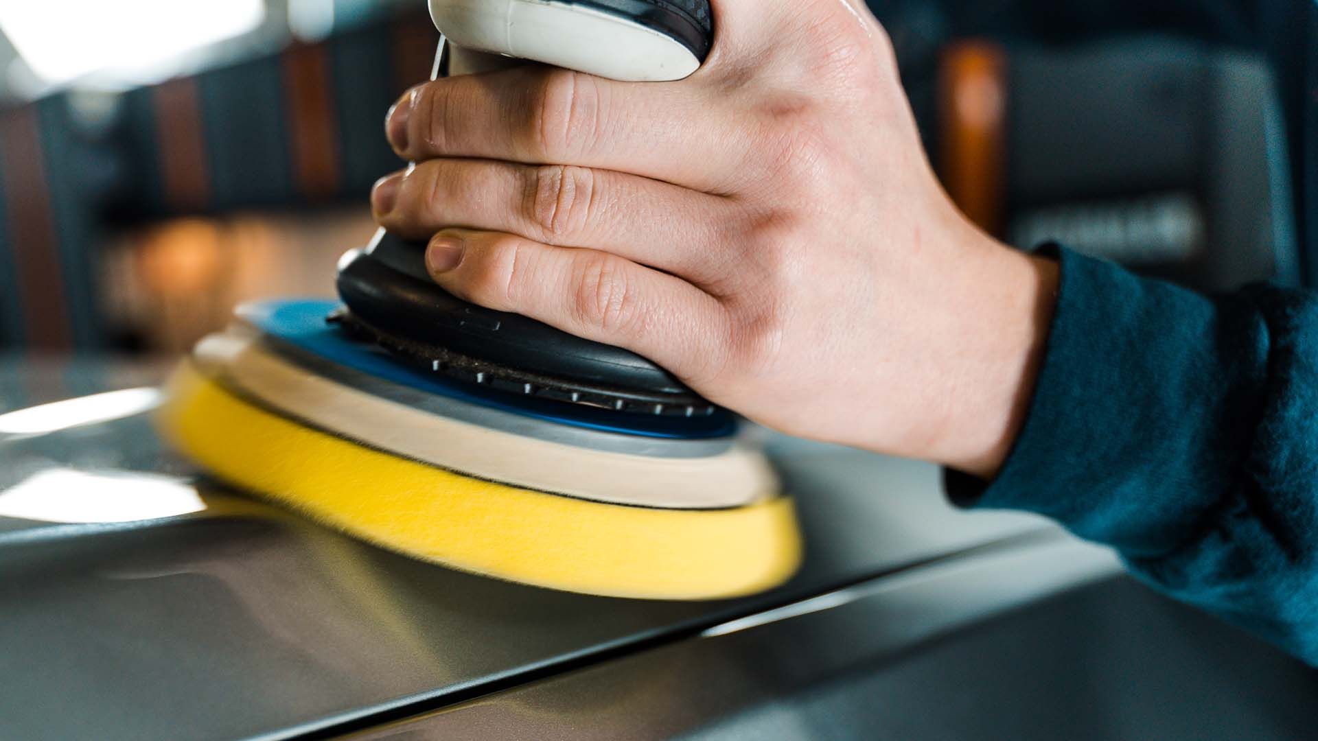 Hand polishing a car hood with a black and yellow buffer pad