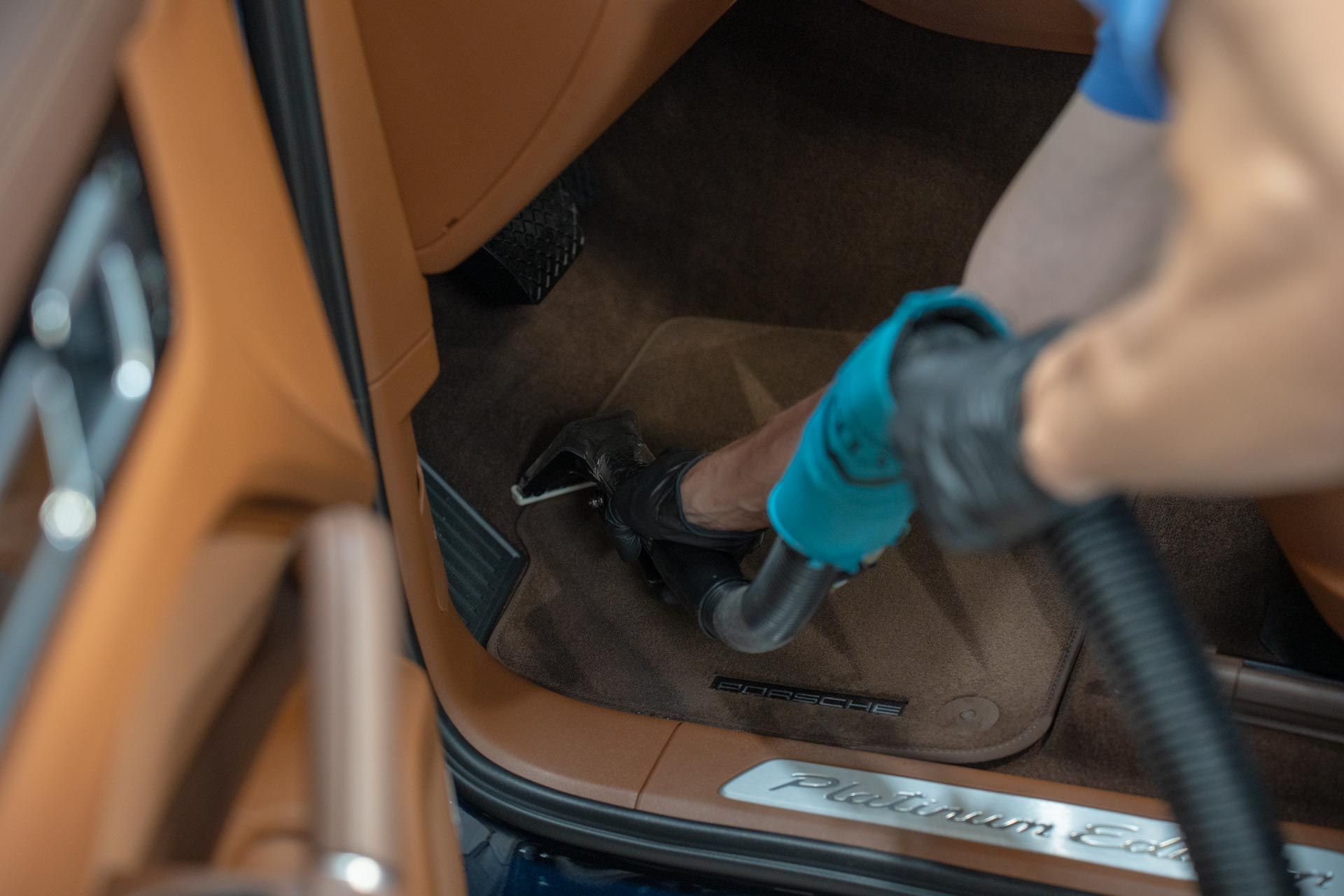 Vacuum cleaner hose cleaning dirt from a car floor mat and footwell