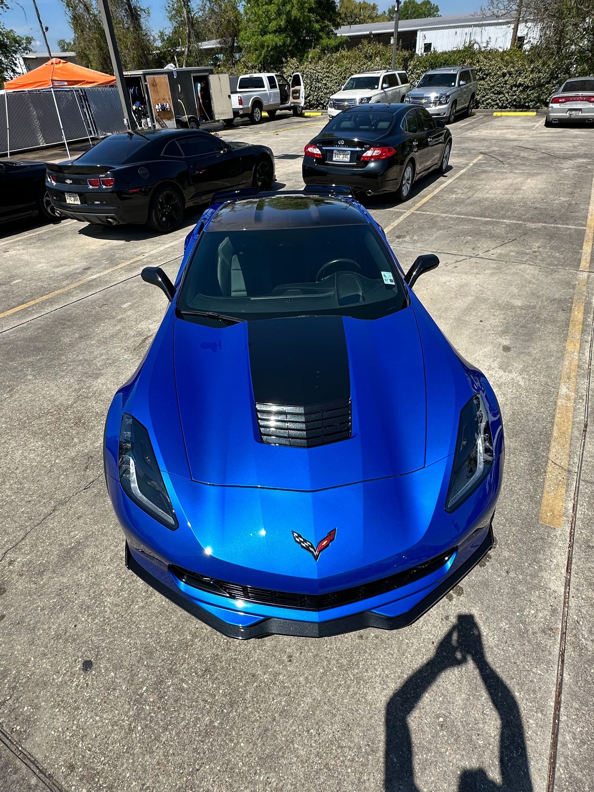 Blue sports car parked in a lot, viewed from above with other cars in the background.