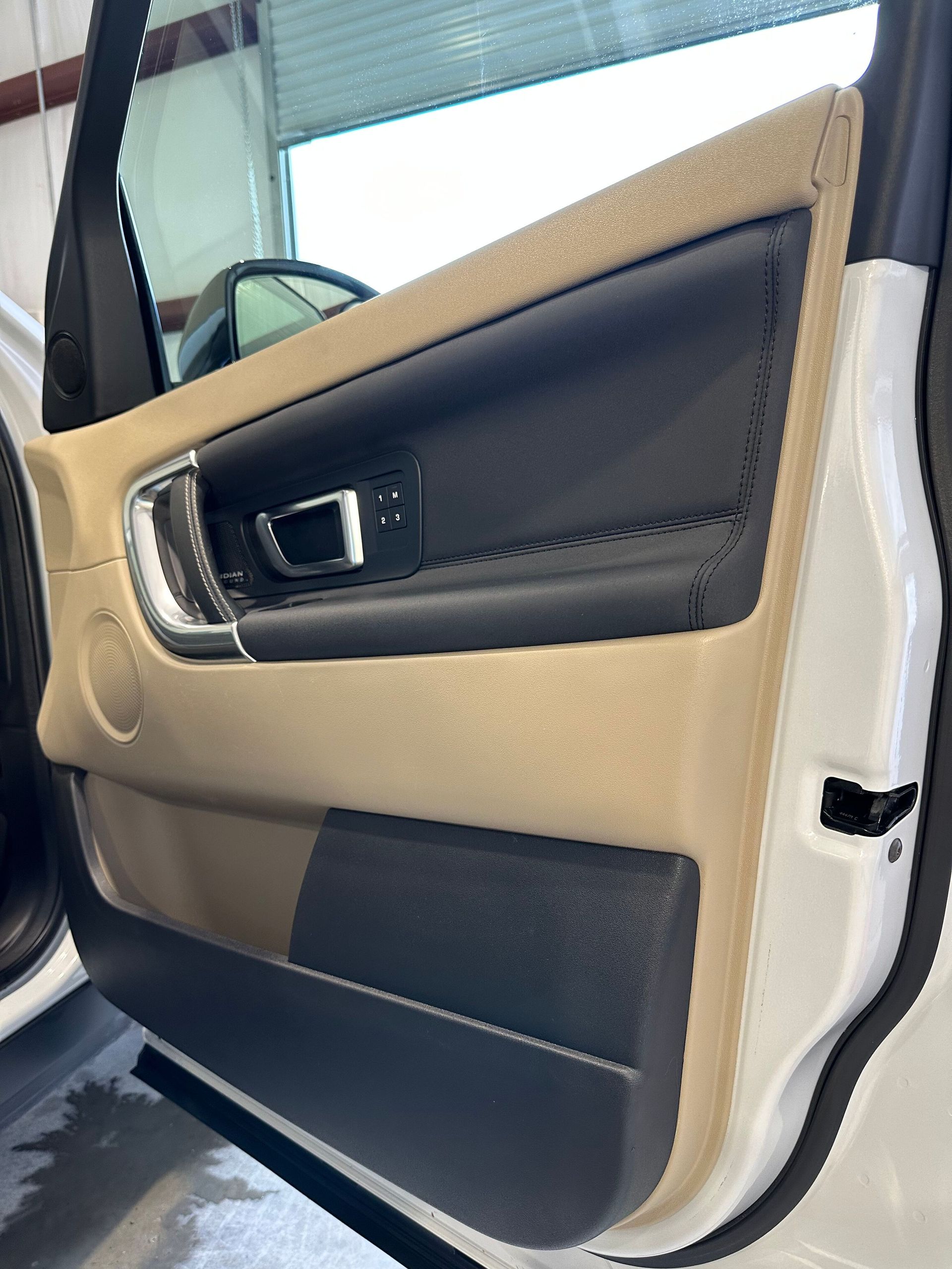 Car door interior panel in beige and black with silver handle and window visible