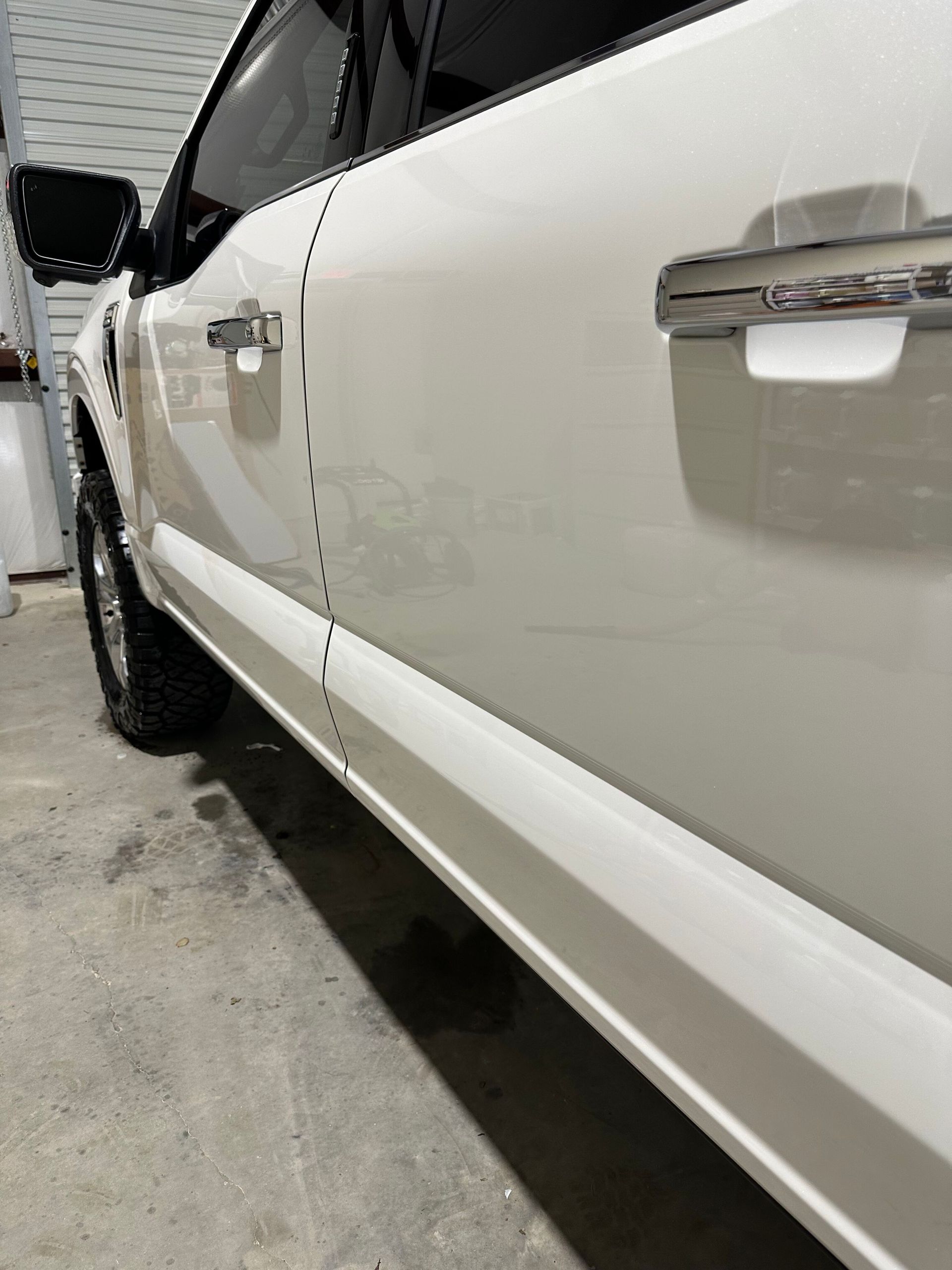 Close-up of a white SUV’s side door and running board in a parking garage