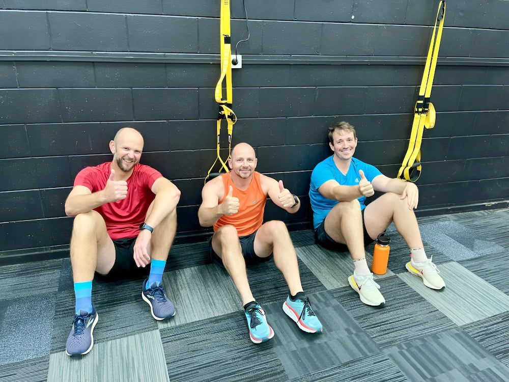 Three Men Are Sitting On The Floor In A Gym Giving Thumbs Up — Ultimate Results Training in Aitkenvale, QLD
