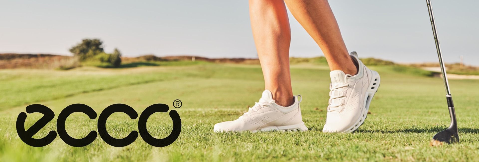 ECCO golfskór á manneskju sem stendur á flötinni, með ECCO merkinu vinstra megin.