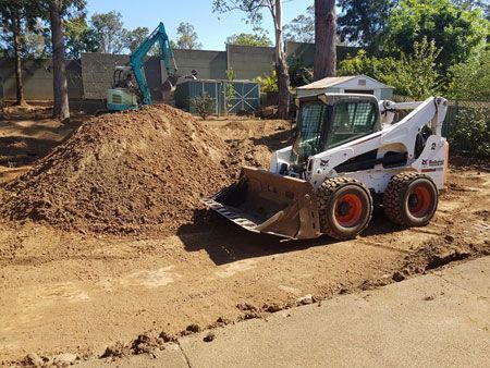 A bulldozer is driving down a dirt road next to a pile of dirt.