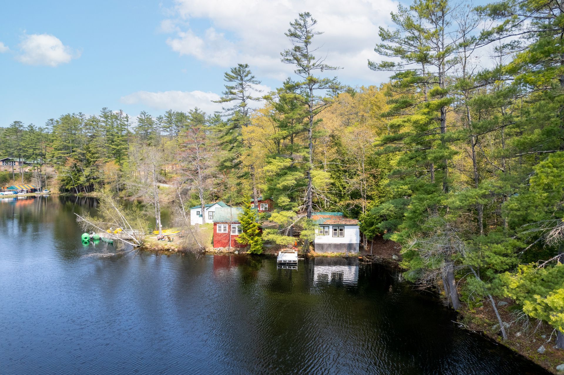 Lakeside cabins surrounded by trees on a sunny day. Red and white buildings with reflections in water.