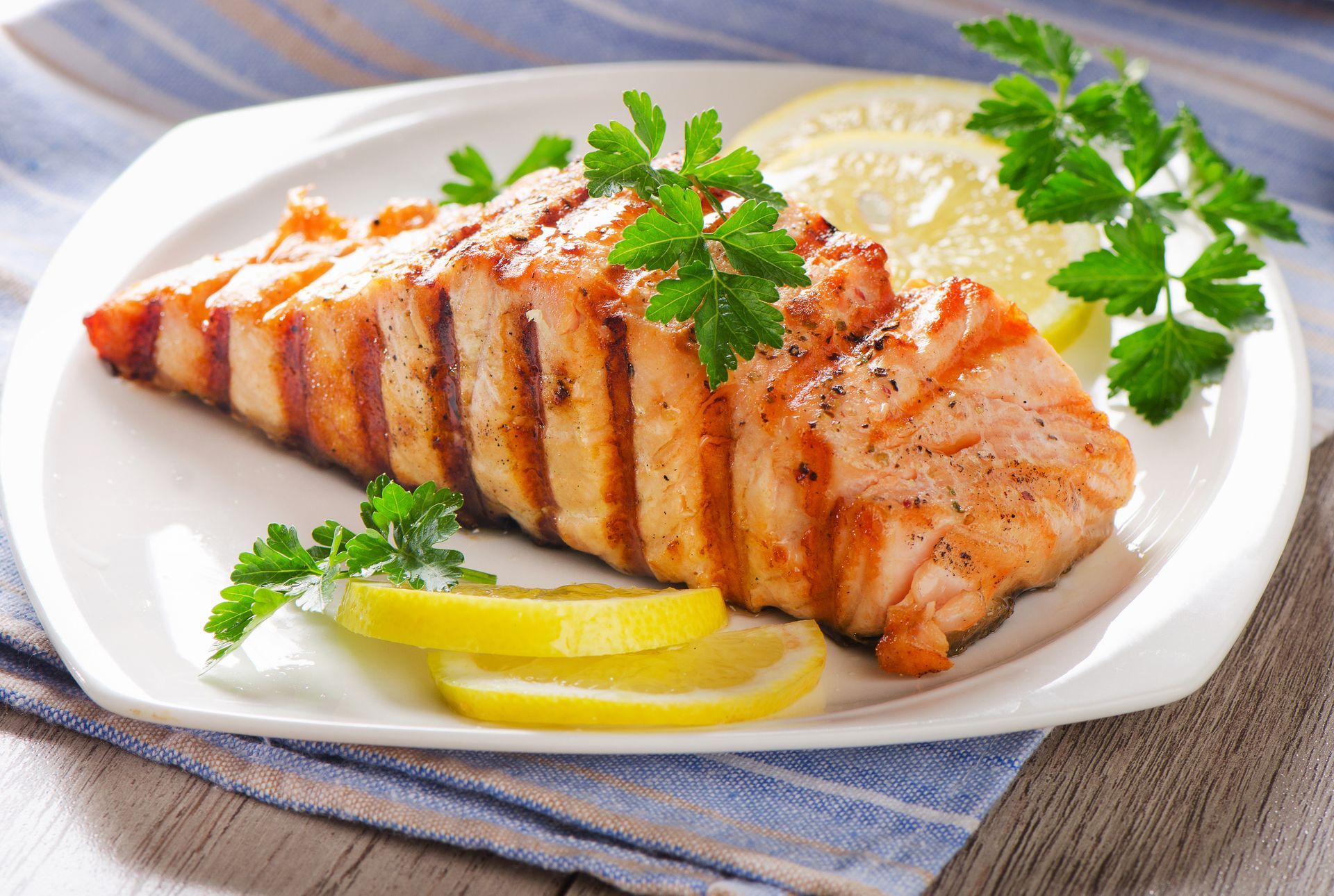 Grilled salmon fillet with lemon slices and parsley on a white plate.