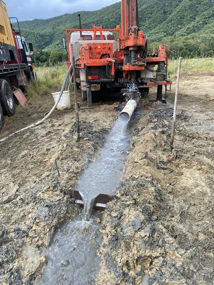 Gloved Hand Holding a Clear Vial of Water Over a Body of Water — FNQ Drilling in Bamboo, QLD