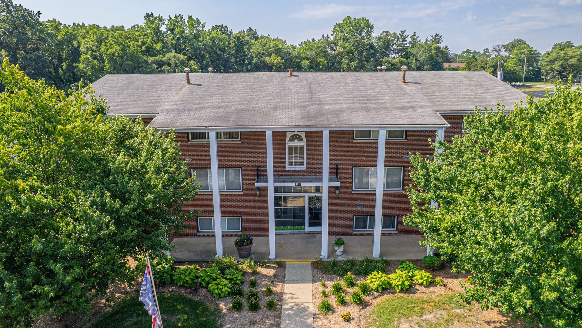 Two-story brick apartment building with white columns and a grassy lawn.