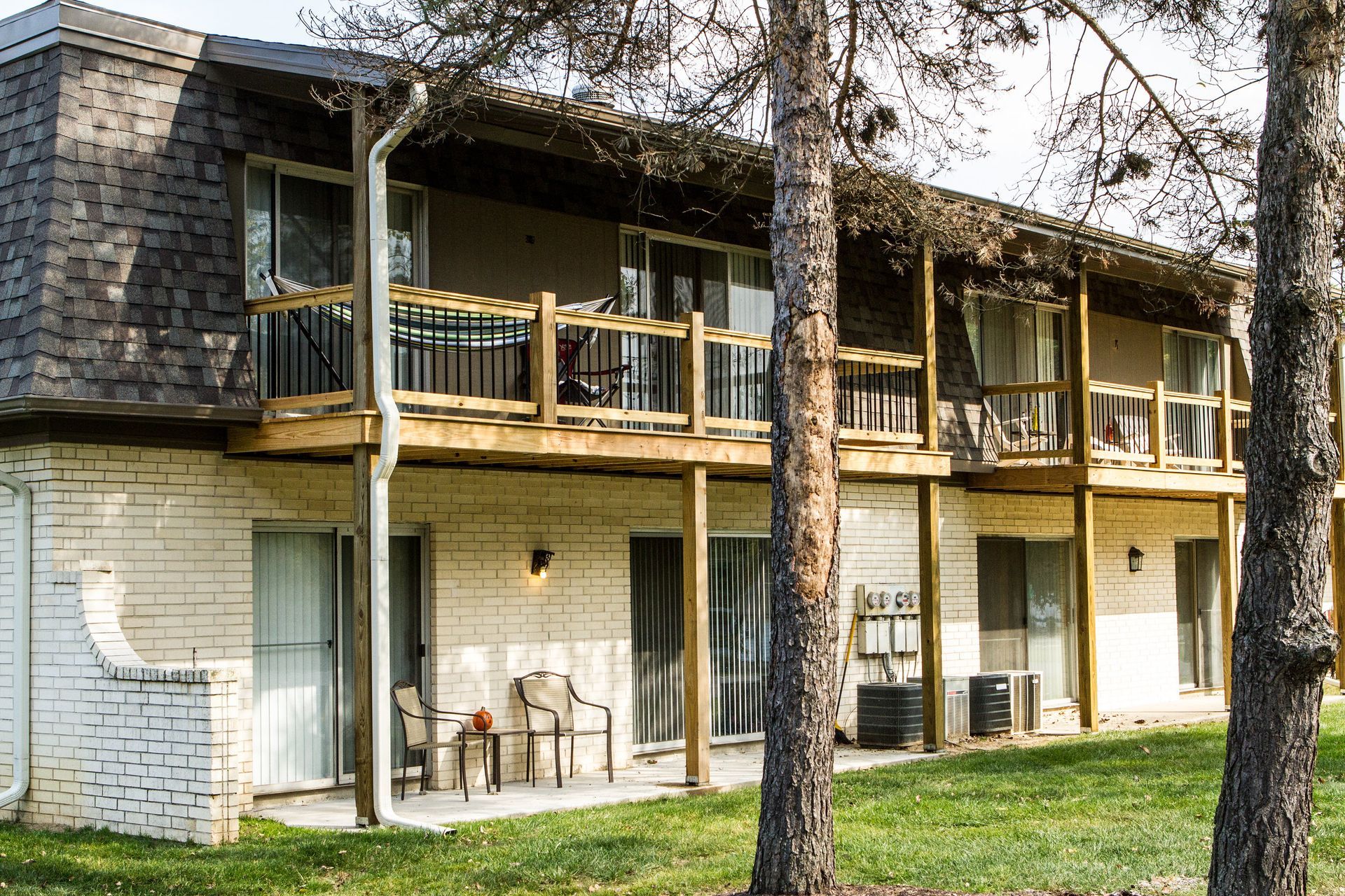 Two-story apartment building with balconies, brick exterior, and a grassy lawn.