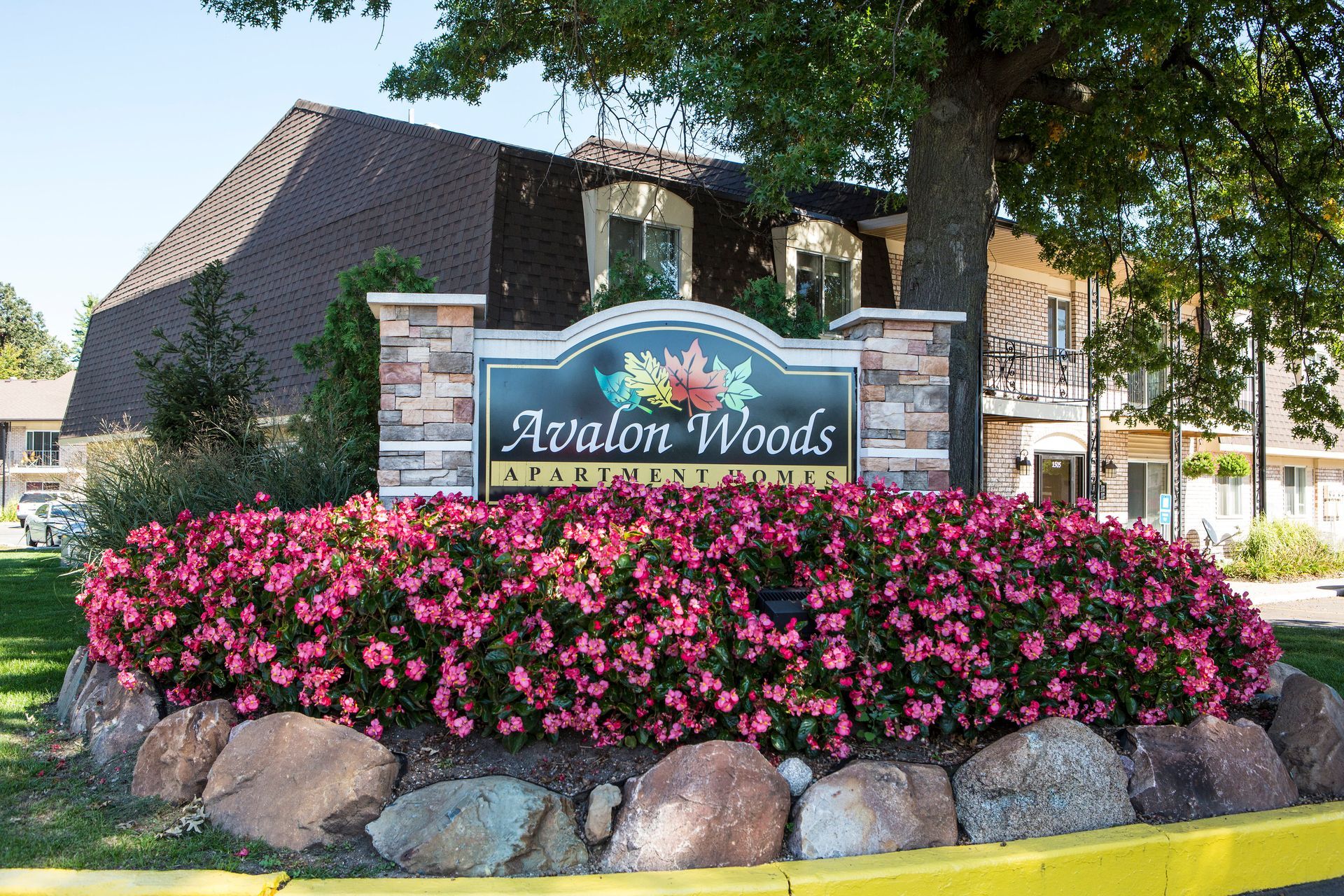 Avalon Woods apartment complex sign with pink flowers and stone accents.