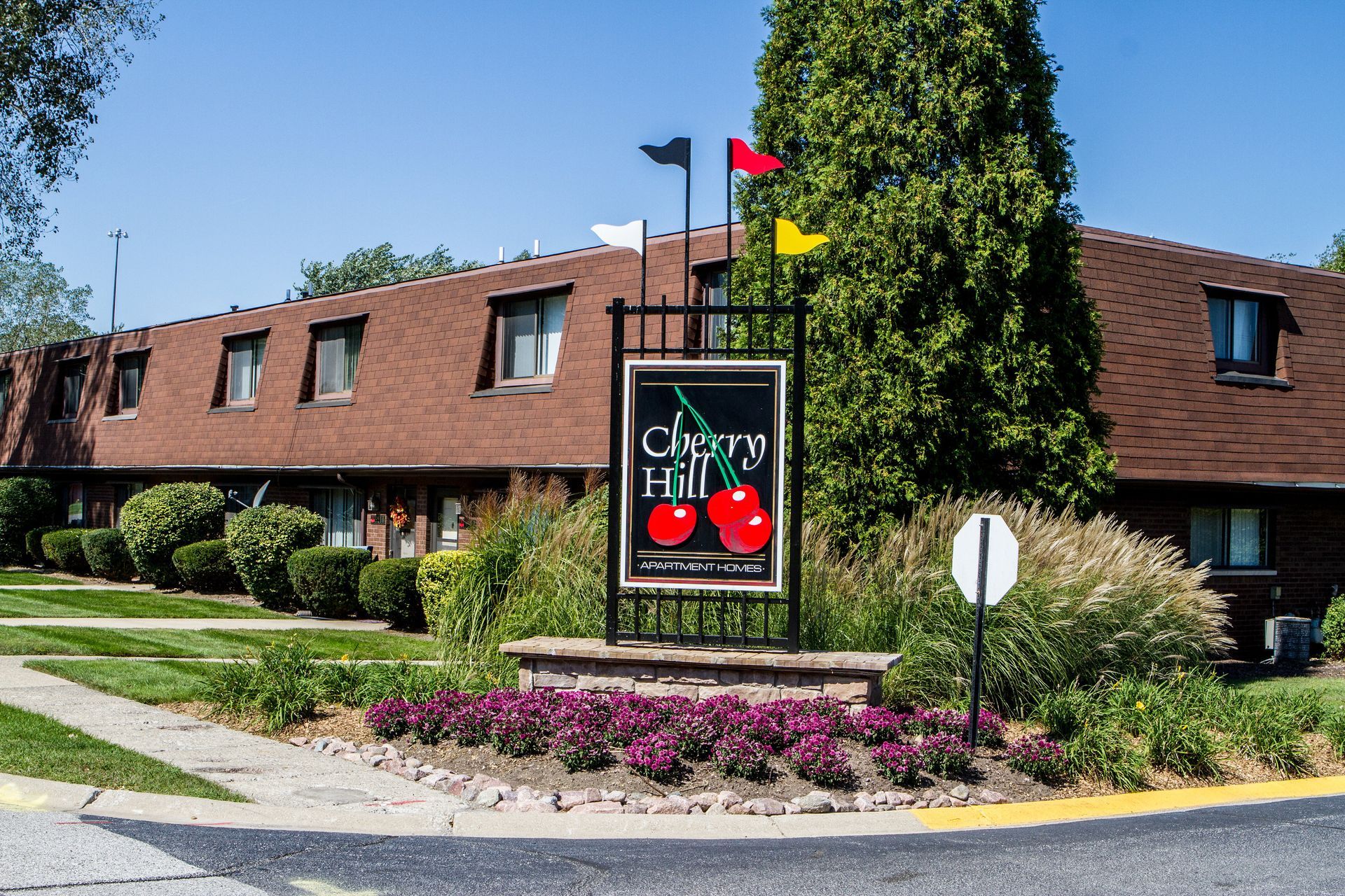 Cherry Hill apartment complex sign with two cherries, flags, and building with brown roof.