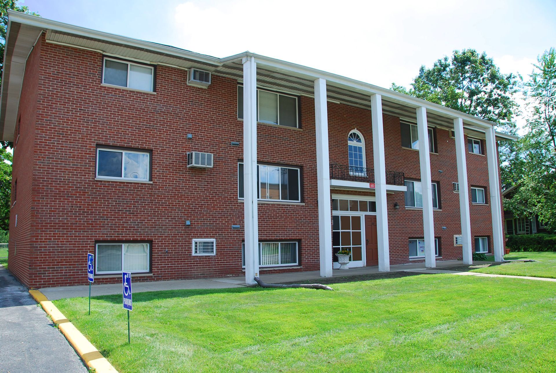 Brick apartment building with white columns and green lawn.