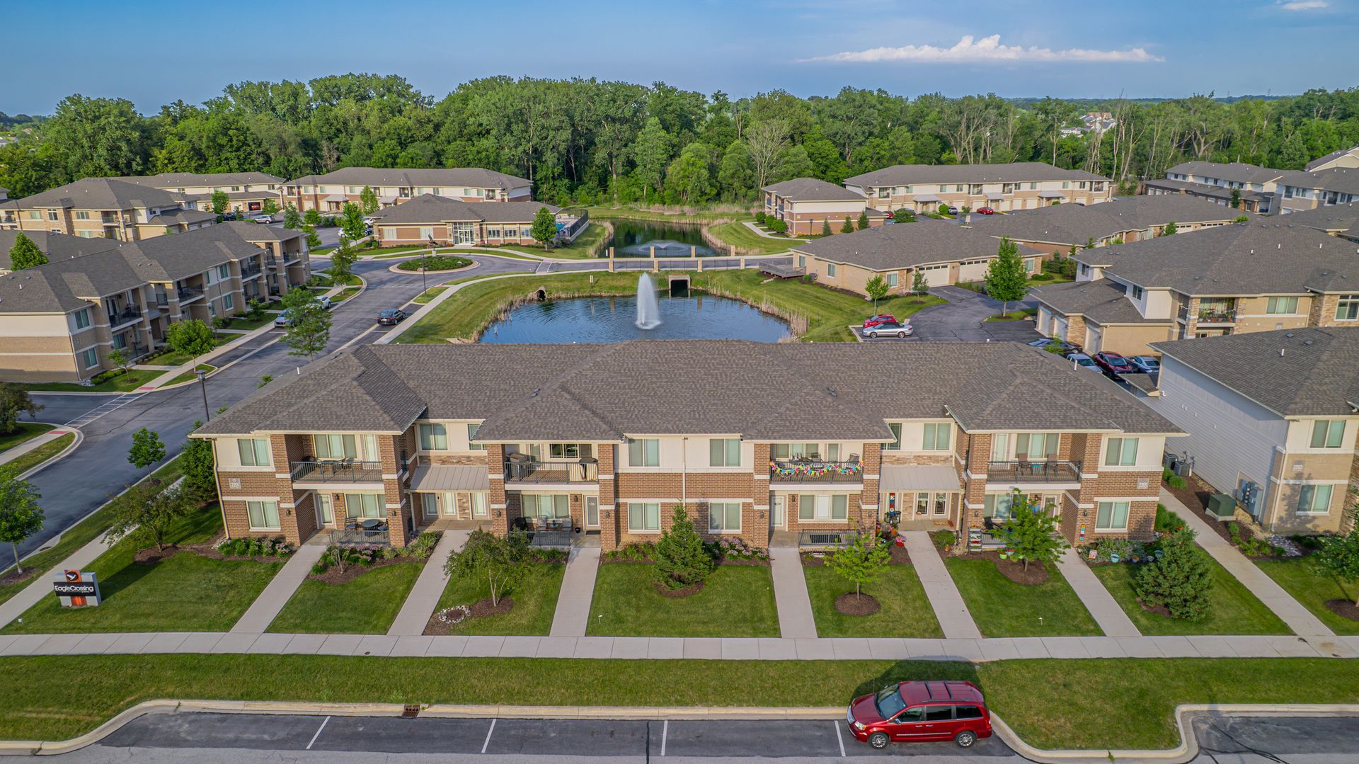 Two-story brick apartment building with balconies, windows, and green lawn on a sunny day.
