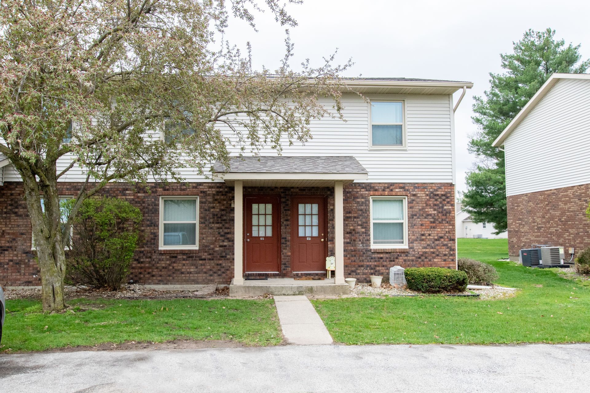 Two-story brick and white-sided duplex with two front doors and small yards on a cloudy day.