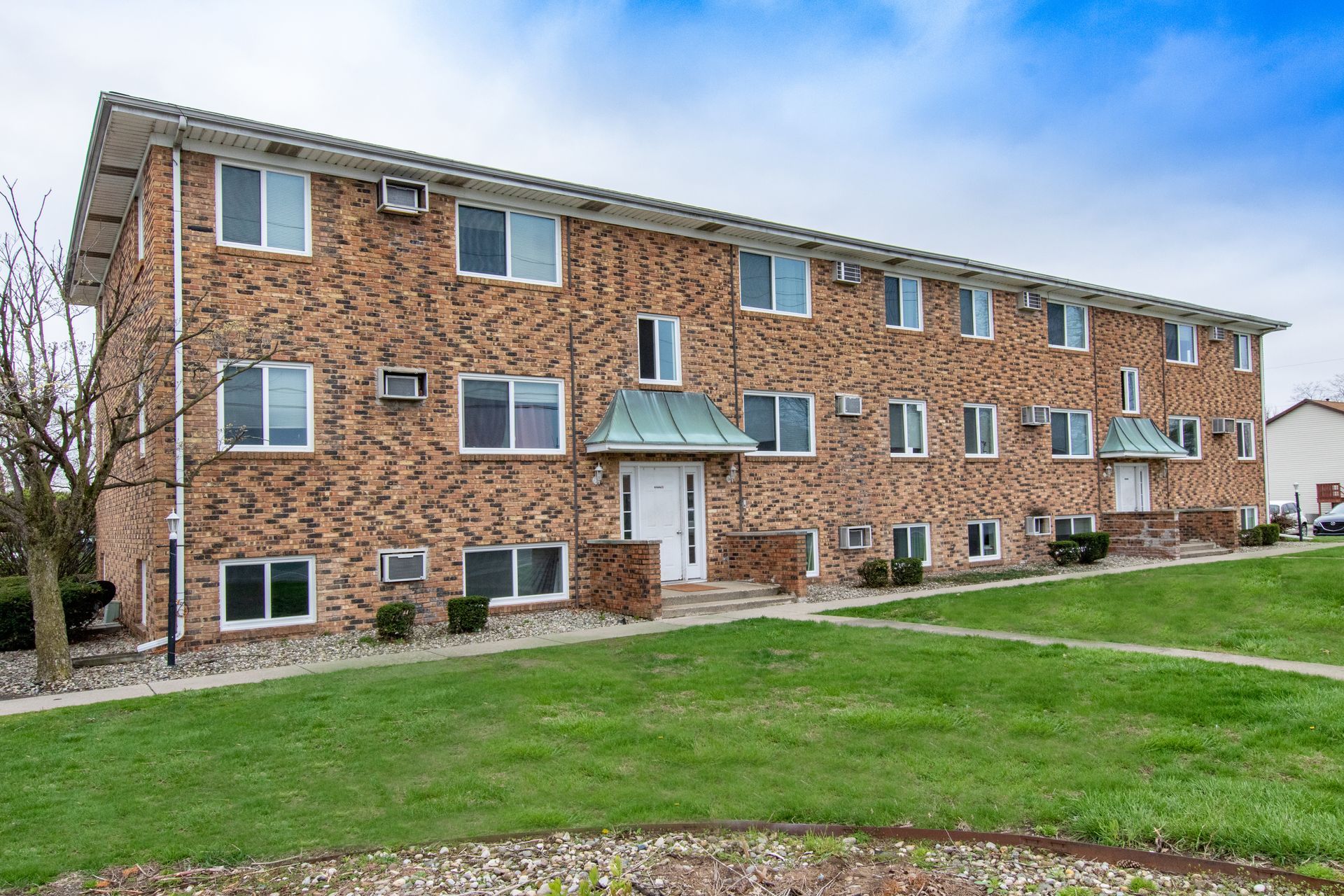 Brick apartment building with white-framed windows and green lawn in front.