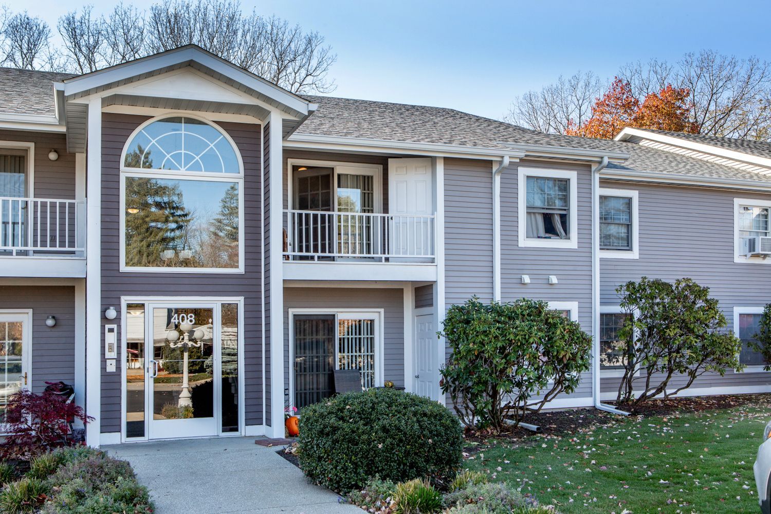Apartment complex with gray siding, white trim, and green lawns on a sunny day.