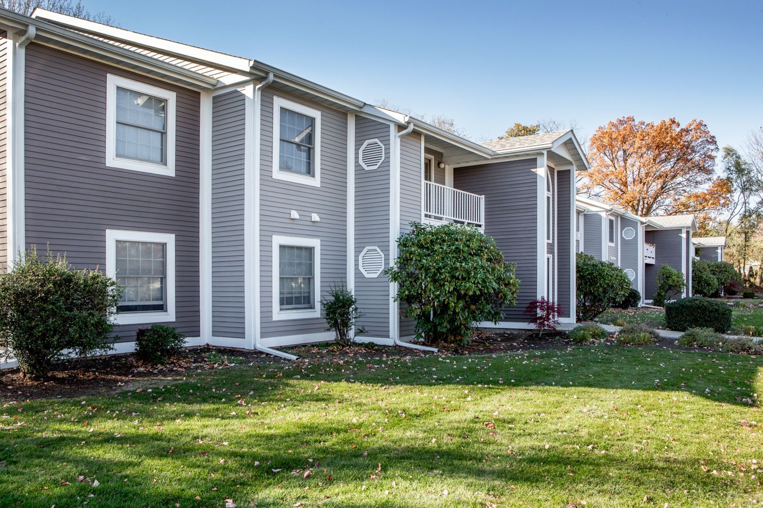 Apartment complex with gray siding, white trim, and green lawns on a sunny day.