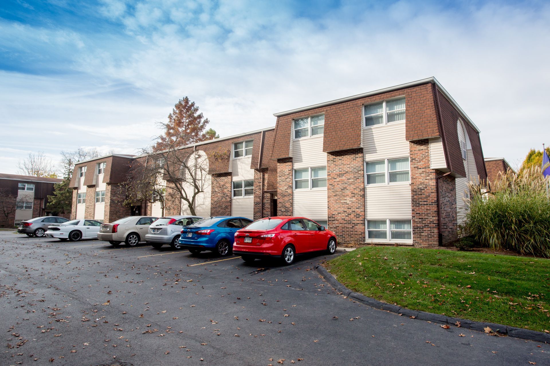 Apartment building with cars parked in front on a cloudy day.