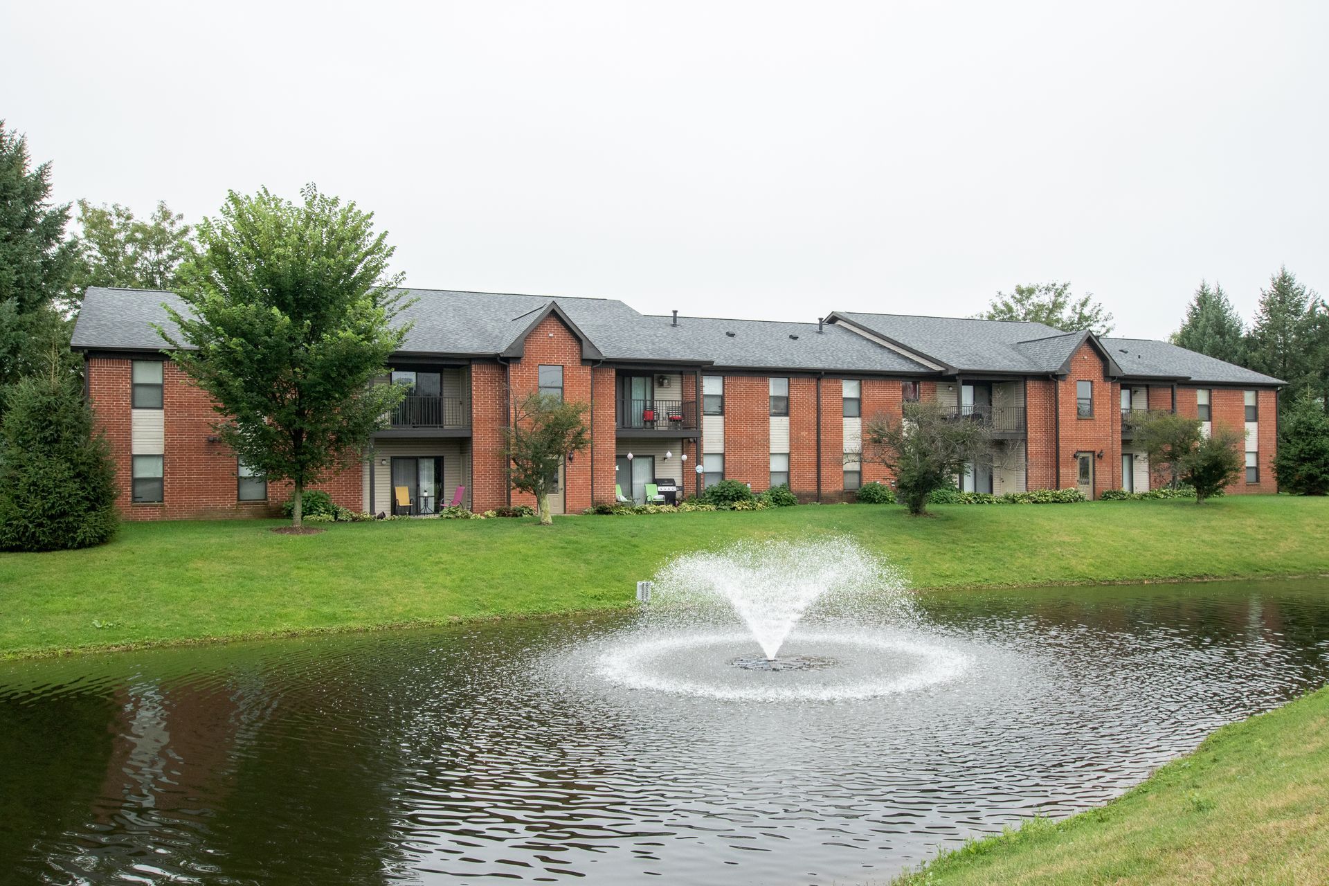 Apartment building with brick exterior, overlooking a pond with a fountain.