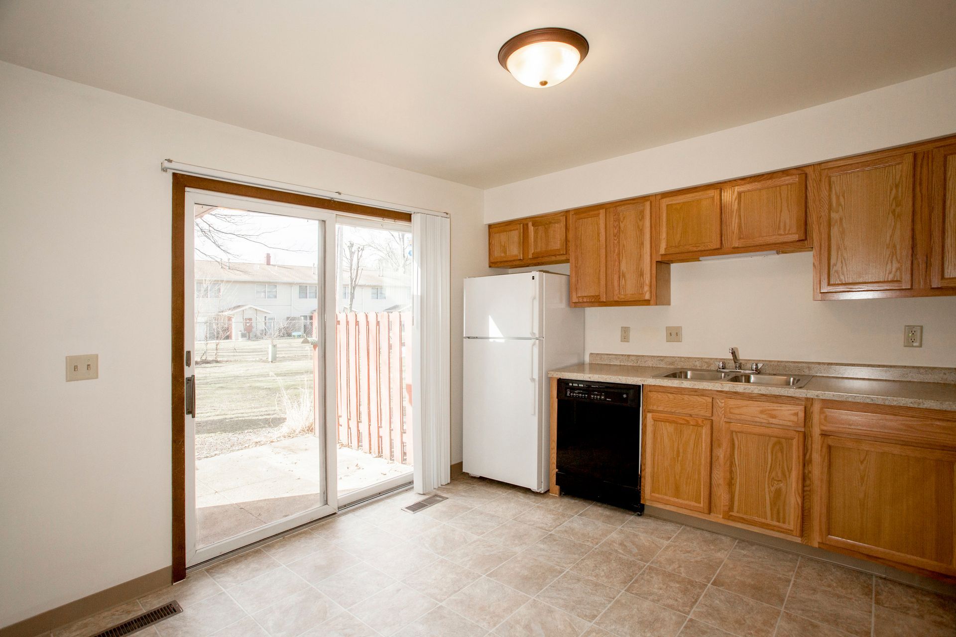 Kitchen with wood cabinets, white appliances, and a sliding glass door to a backyard.